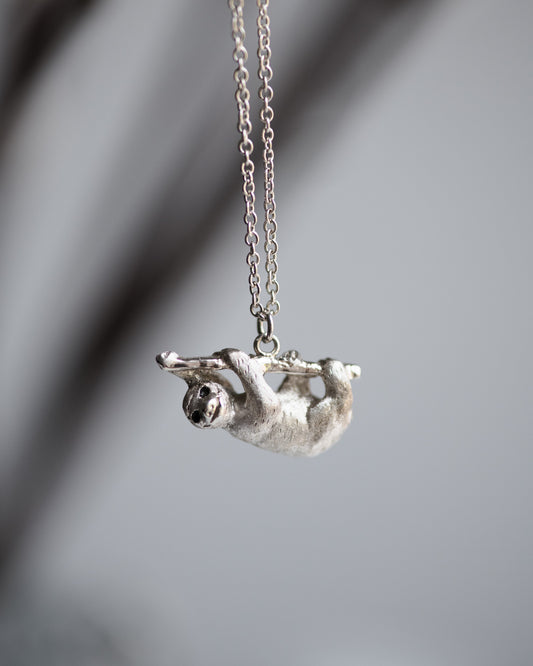 Silver sloth pendant on a chain against a blurred gray background