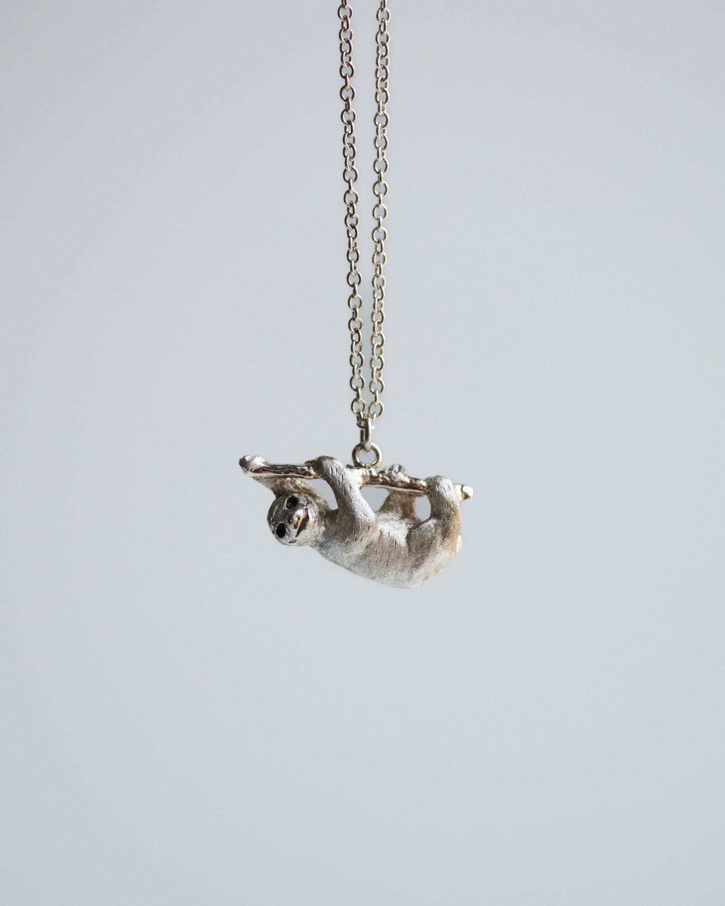 Silver sloth pendant on a chain against a light gray background