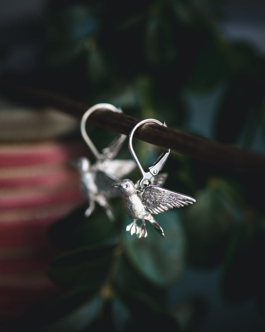 Hand carved Silver songbird earrings on a dark background