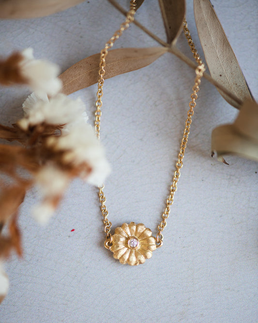 Gold bracelet with a daisy pendant with a diamond on a light background