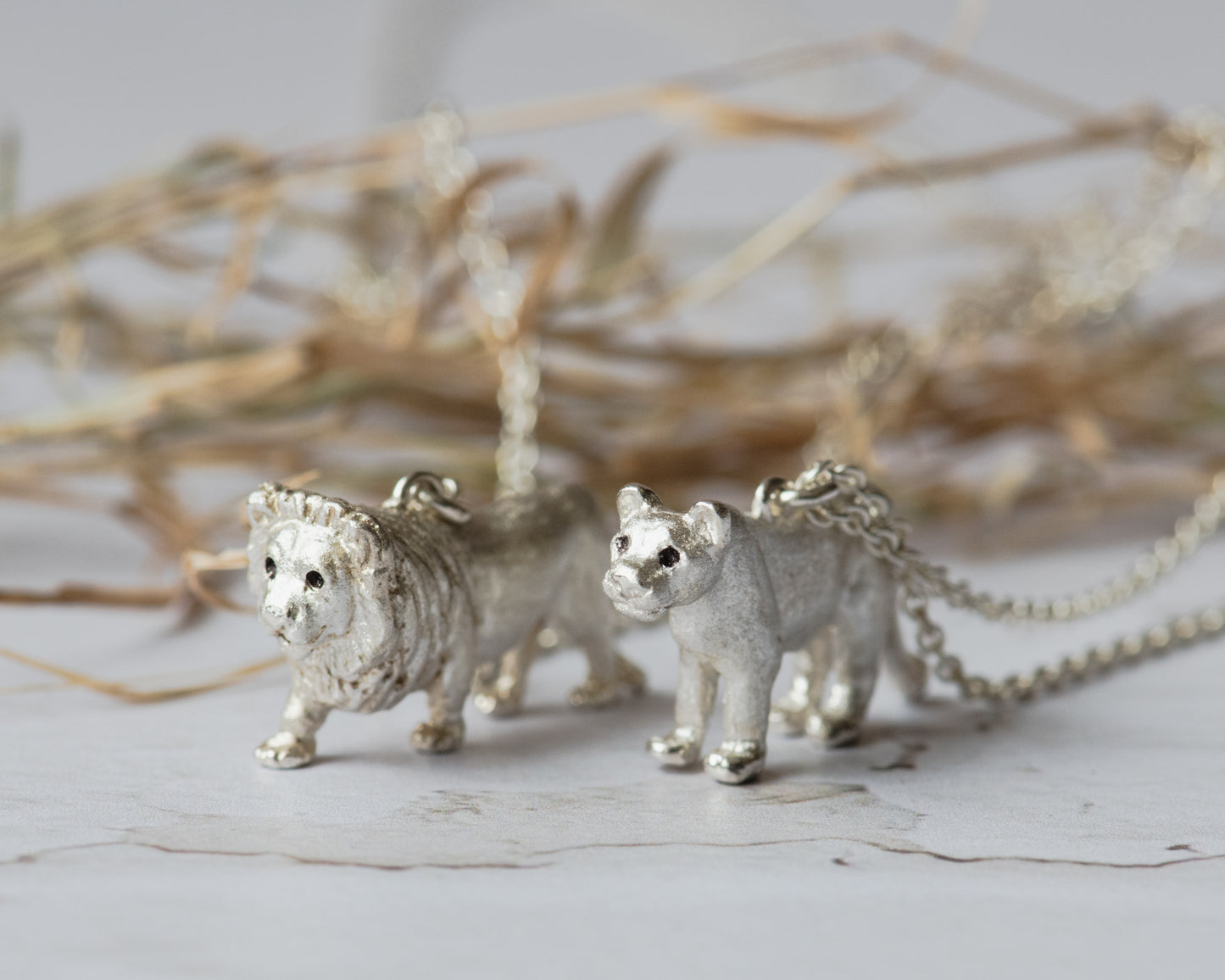 Silver lion and lioness pendants on chains against a neutral background