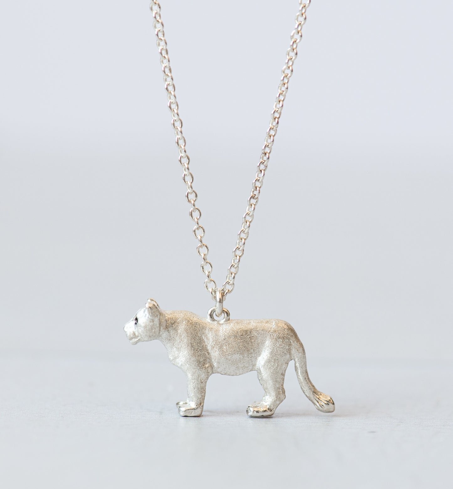 Silver lioness pendant on a chain against a light gray background