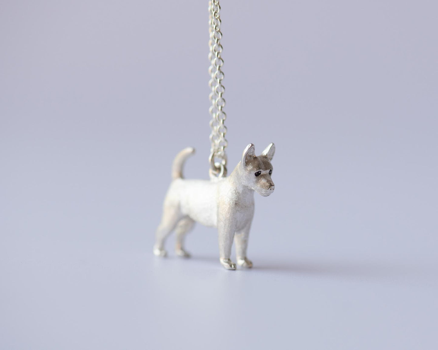 Dog-shaped pendant on a chain against a light gray background