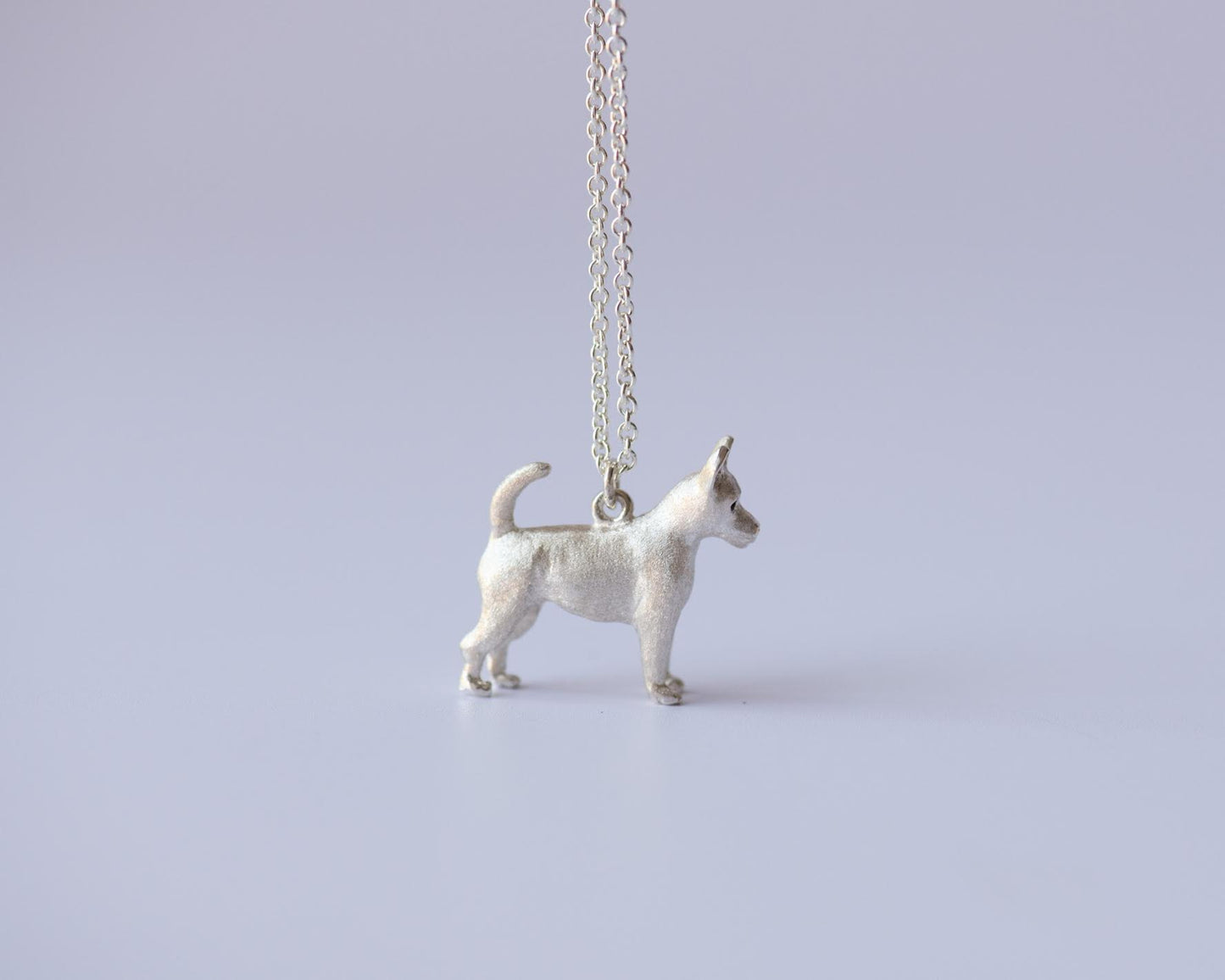 Silver chihuahua pendant on a chain against a light purple background