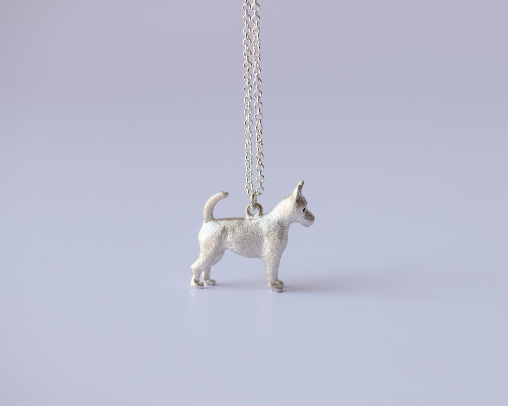 Silver chihuahua pendant on a chain against a light purple background