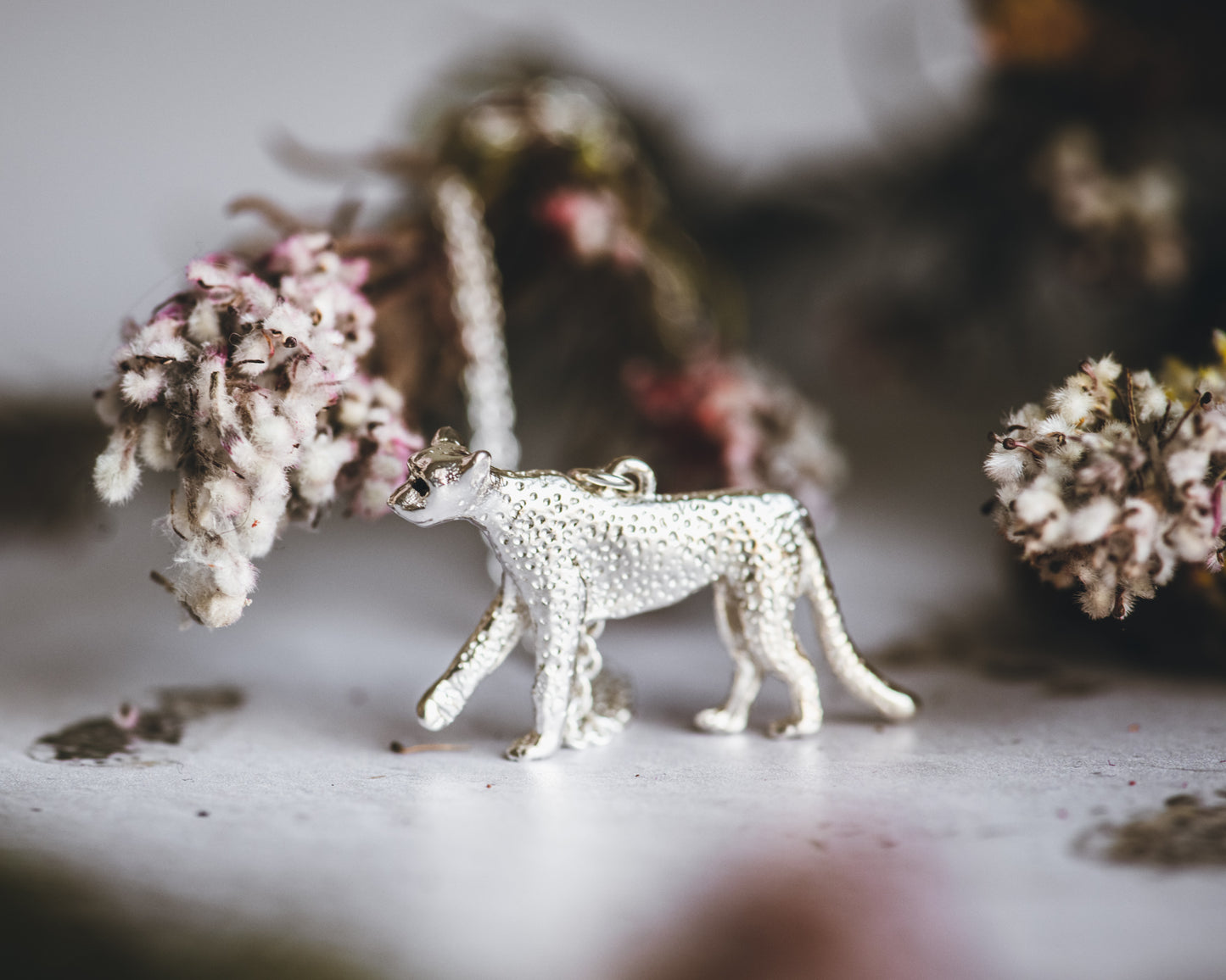 Silver cheetah figurine on a textured surface with blurred natural elements in the background