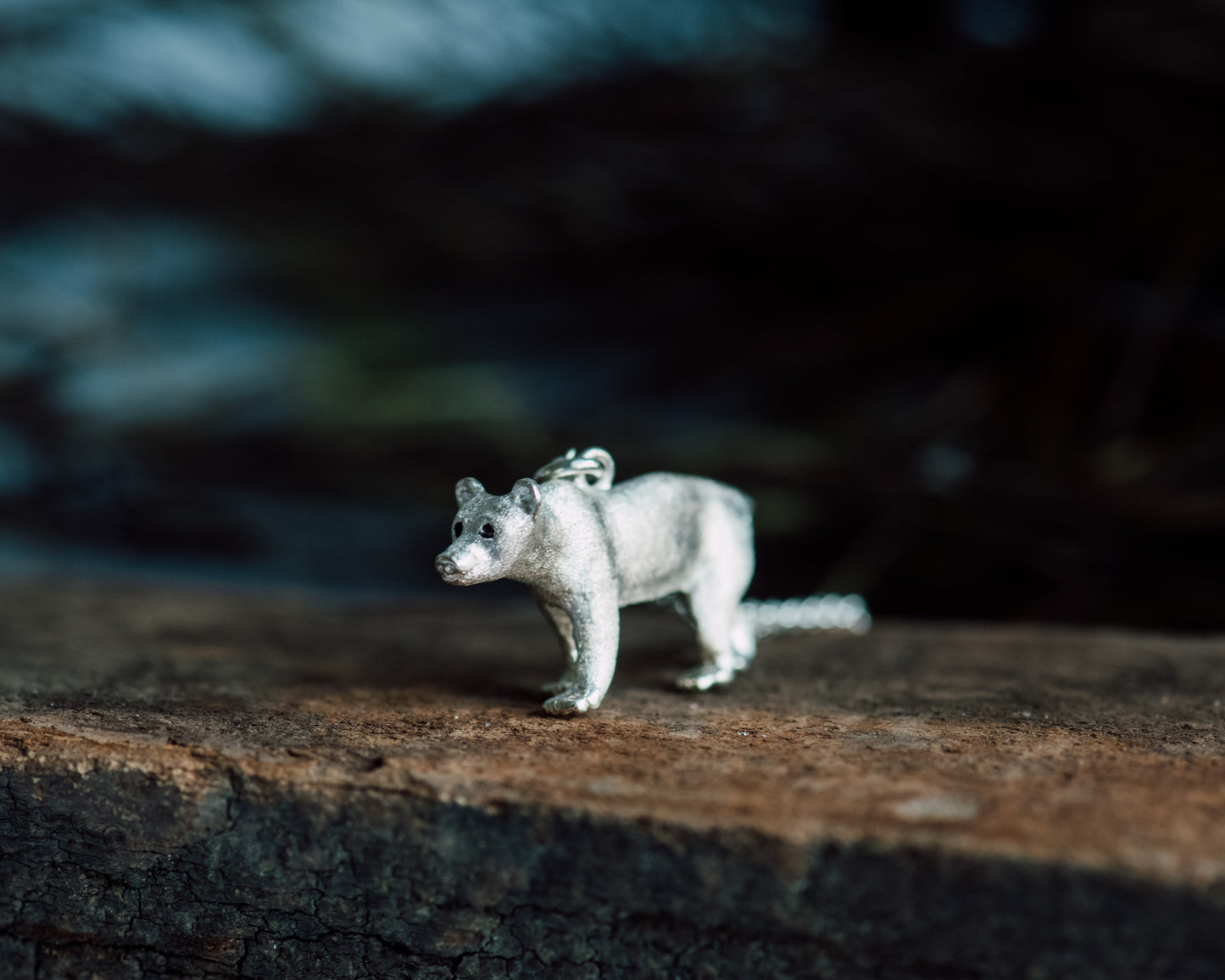 Silver bear figurine on a dark stone surface with a blurred natural background