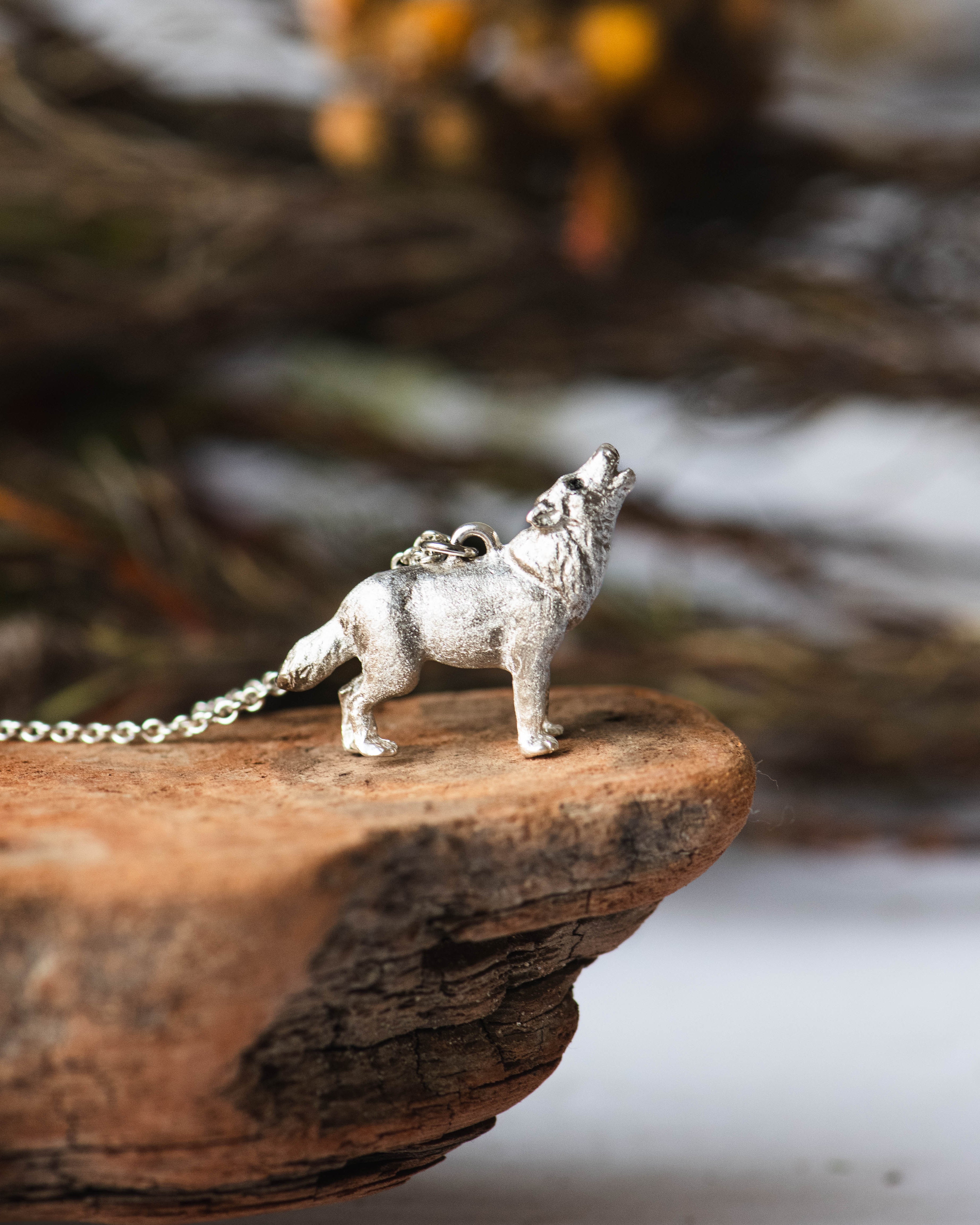 Silver wolf necklace on a wooden surface with a blurred natural background