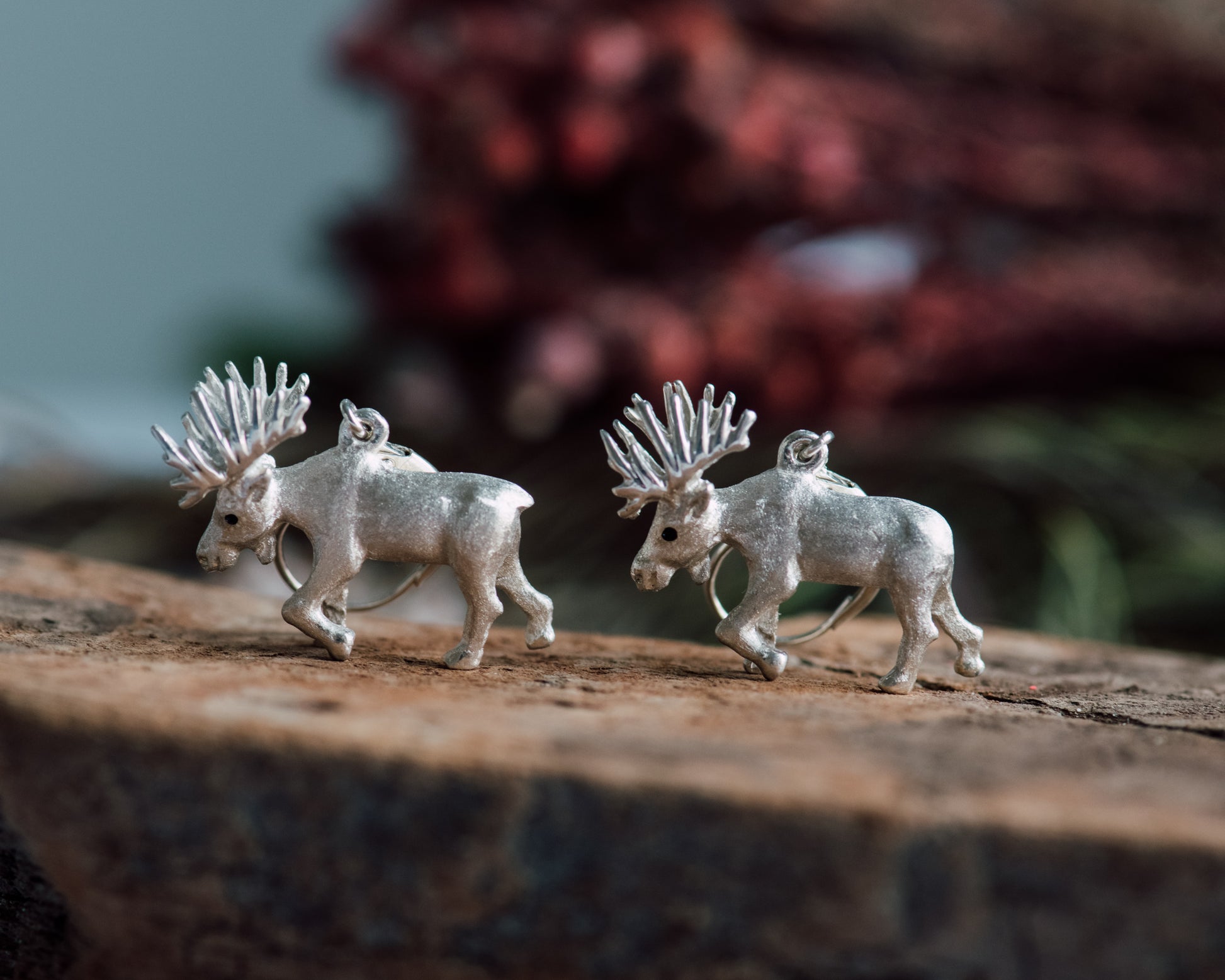 Silver moose-shaped earrings on a wooden surface with a blurred natural background
