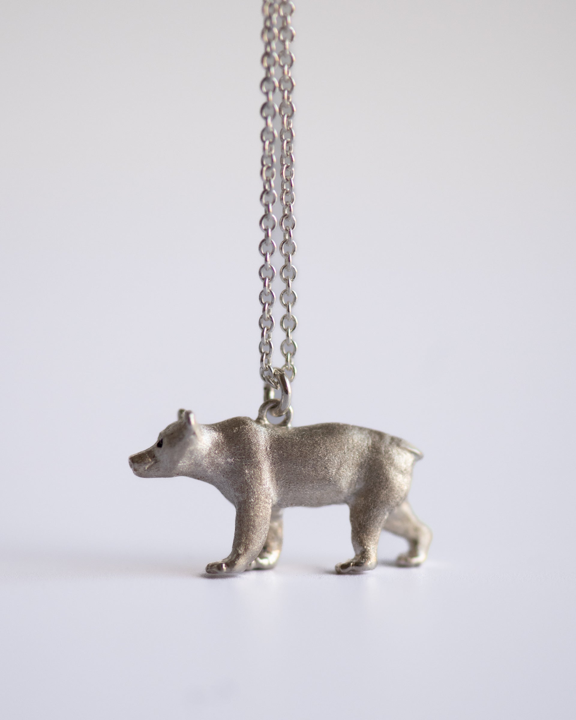 Silver bear pendant on a chain against a white background