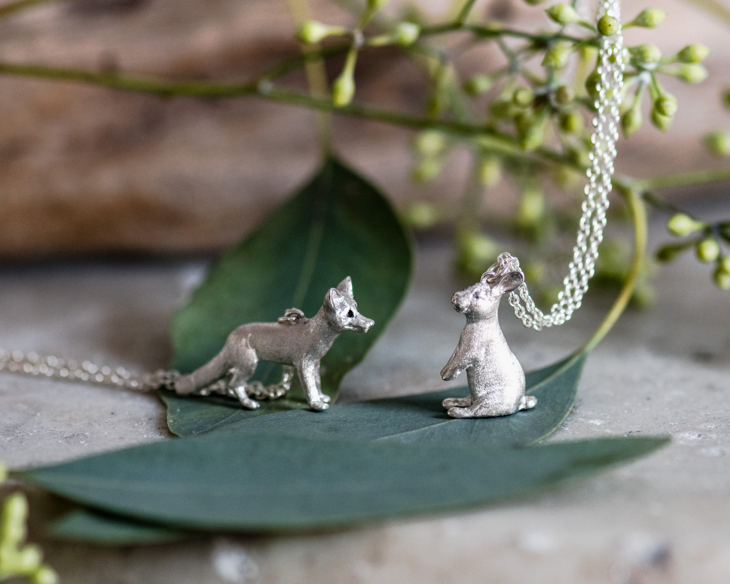 Silver fox and rabbit pendant on a chain with a green leaf and natural background