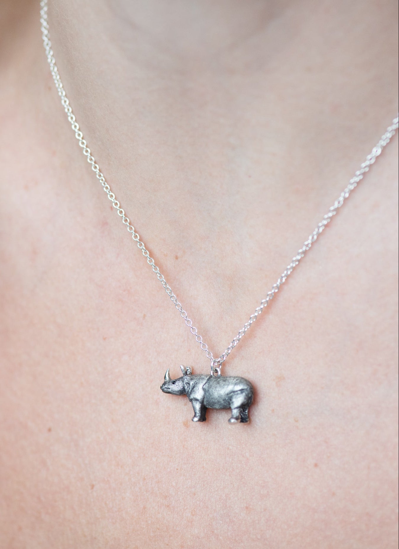 Silver rhinoceros pendant necklace on a person's neck