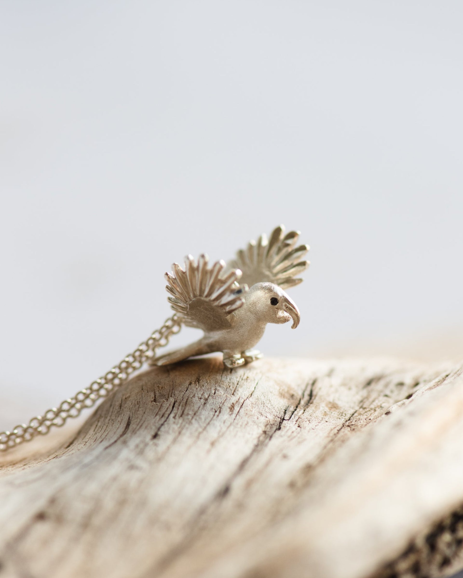 Bird-shaped macaw pendant on a chain with a natural wood background