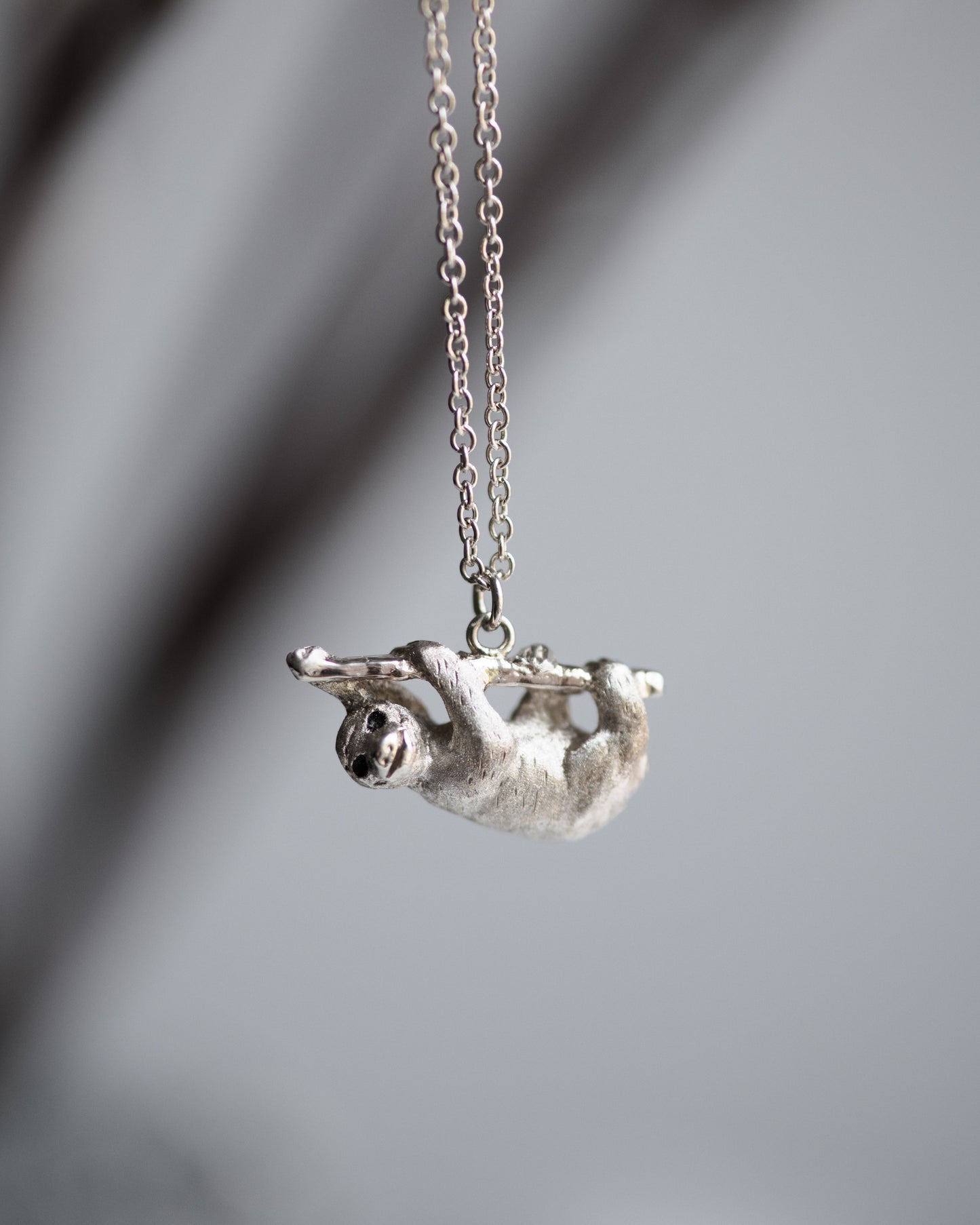 Silver sloth pendant on a chain against a blurred gray background