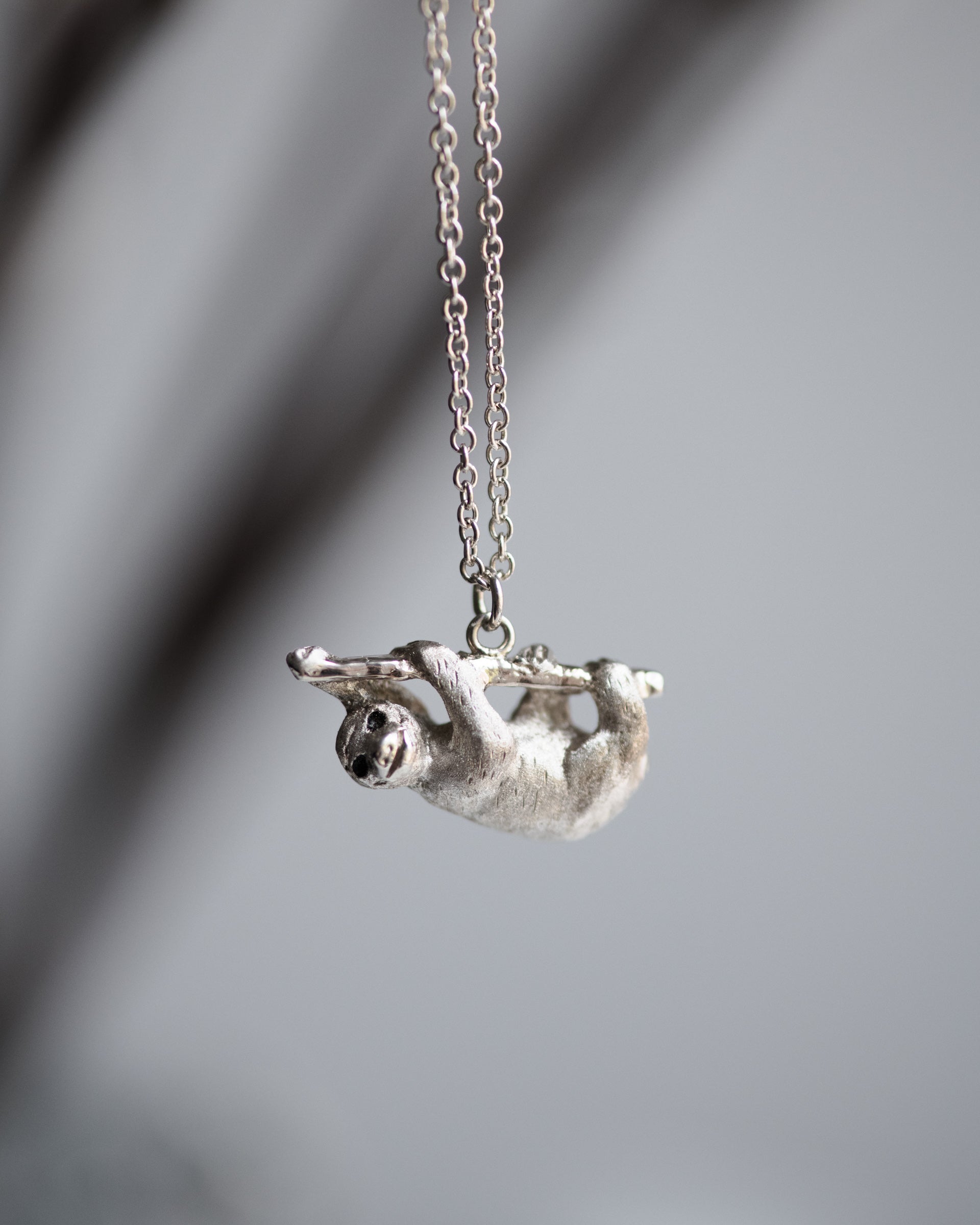 Silver sloth pendant on a chain against a blurred gray background
