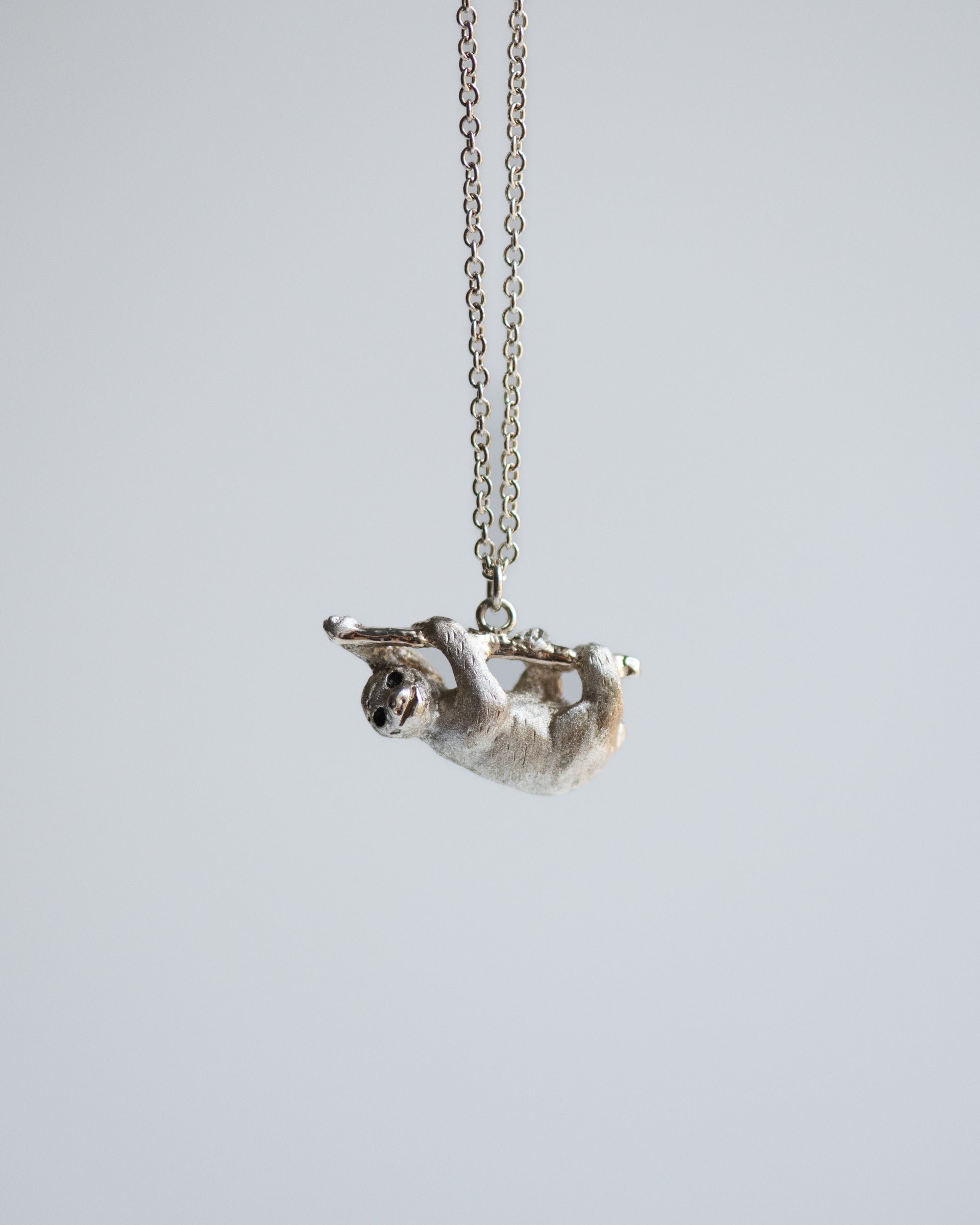 Silver sloth pendant on a chain against a light gray background