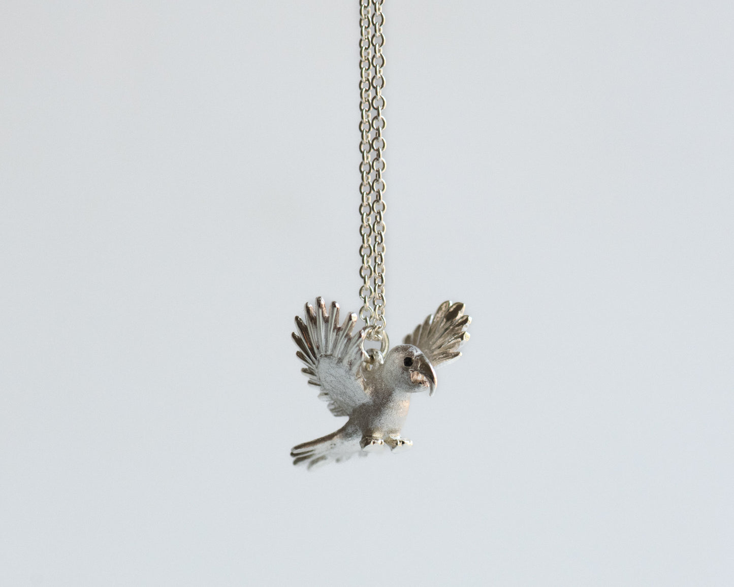 Silver macaw bird pendant on a chain against a light gray background