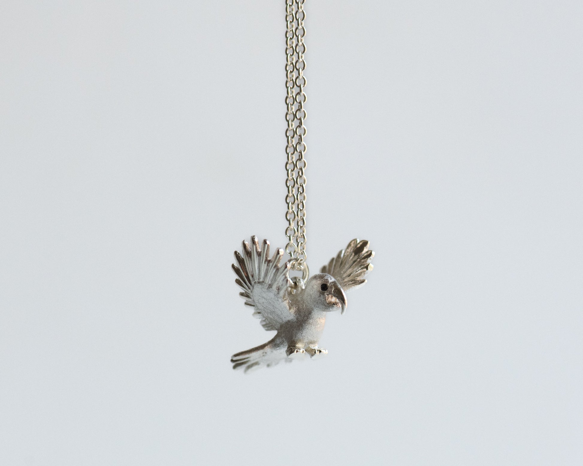 Silver macaw bird pendant on a chain against a light gray background