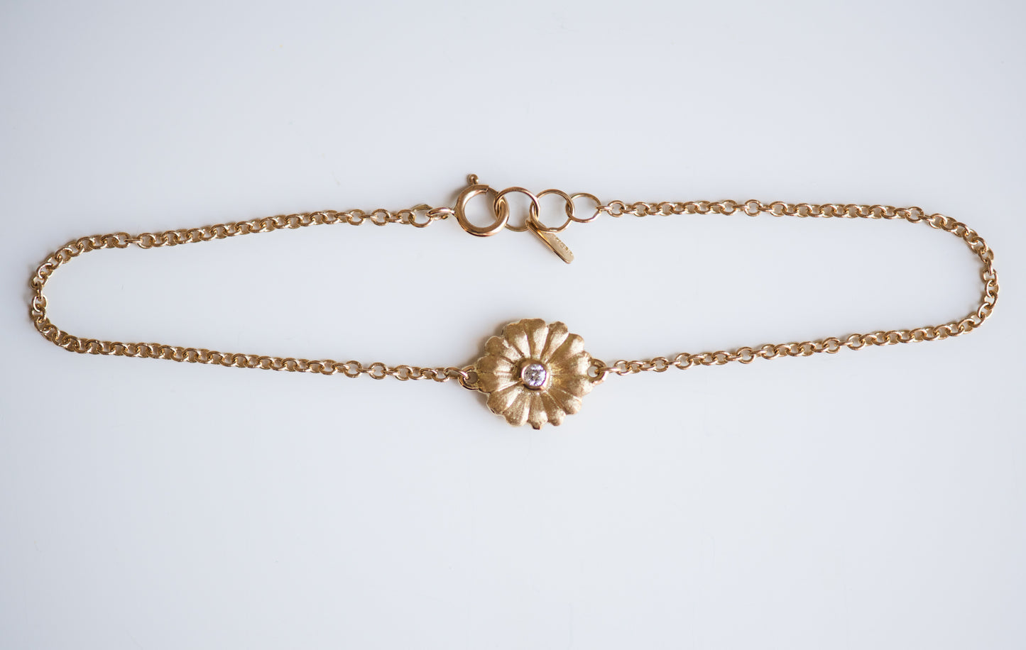Gold bracelet with a daisy and a diamond  on a light gray background