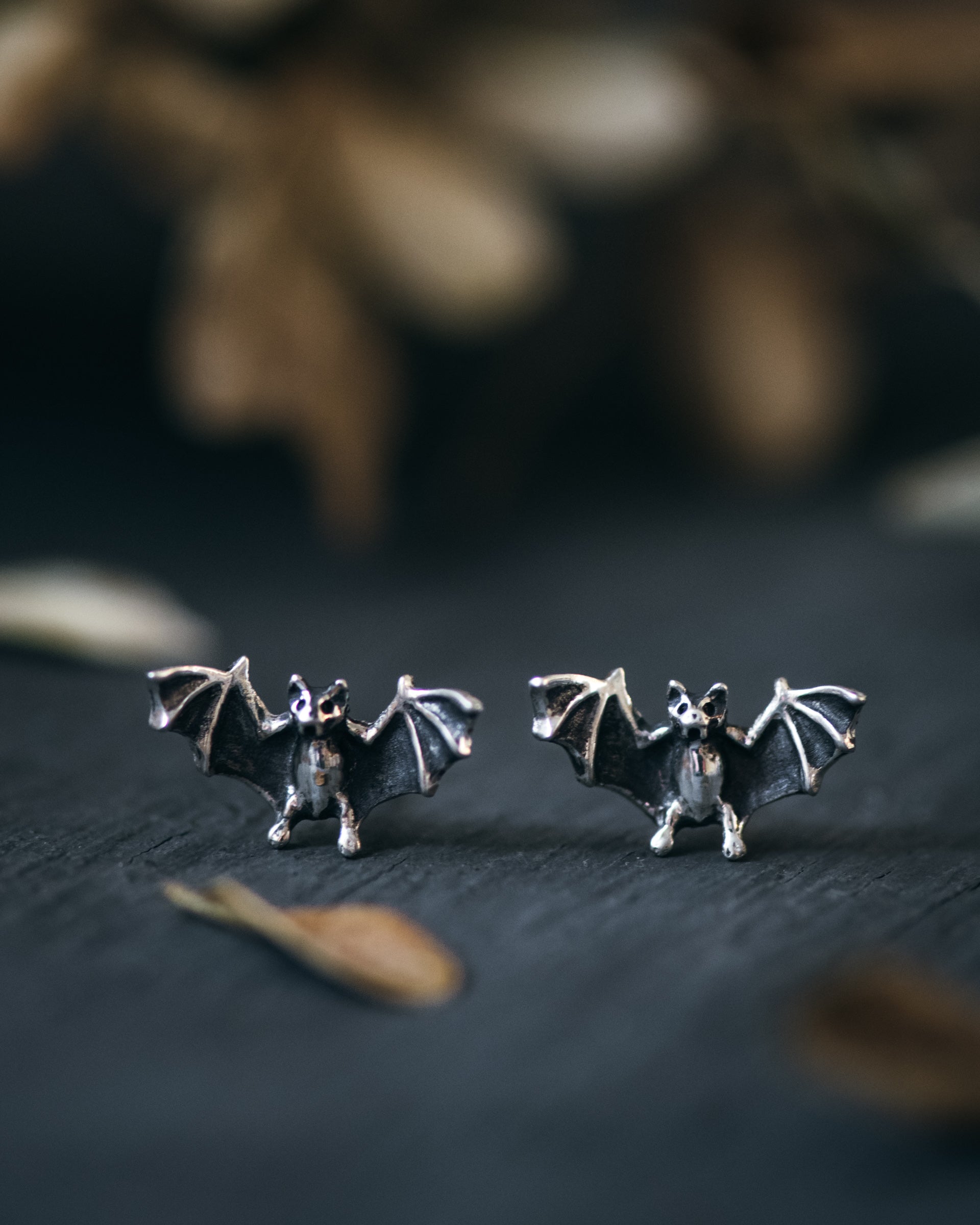Bat-shaped earrings on a dark surface with a blurred natural background