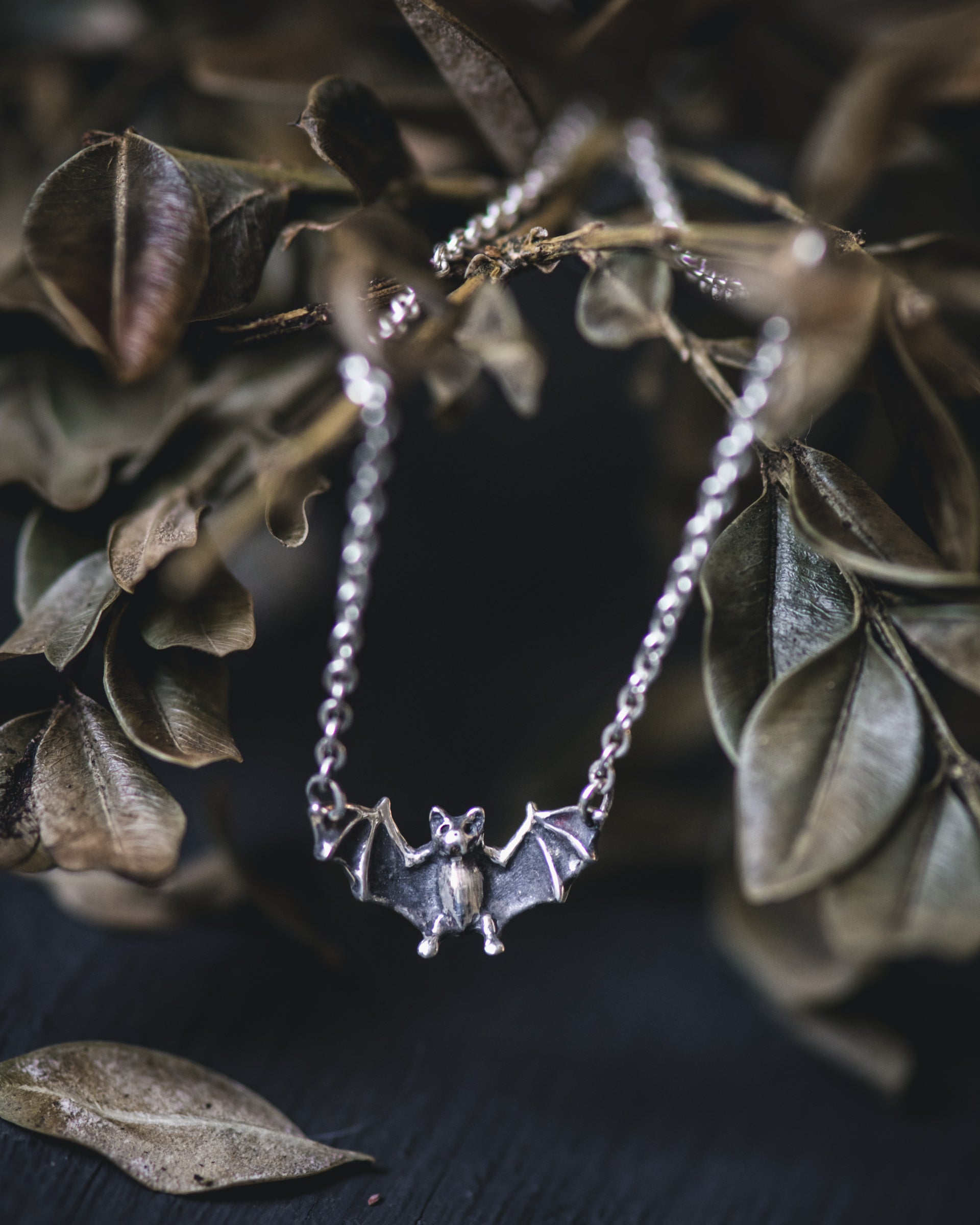 Silver bat necklace on a dark background with leaves
