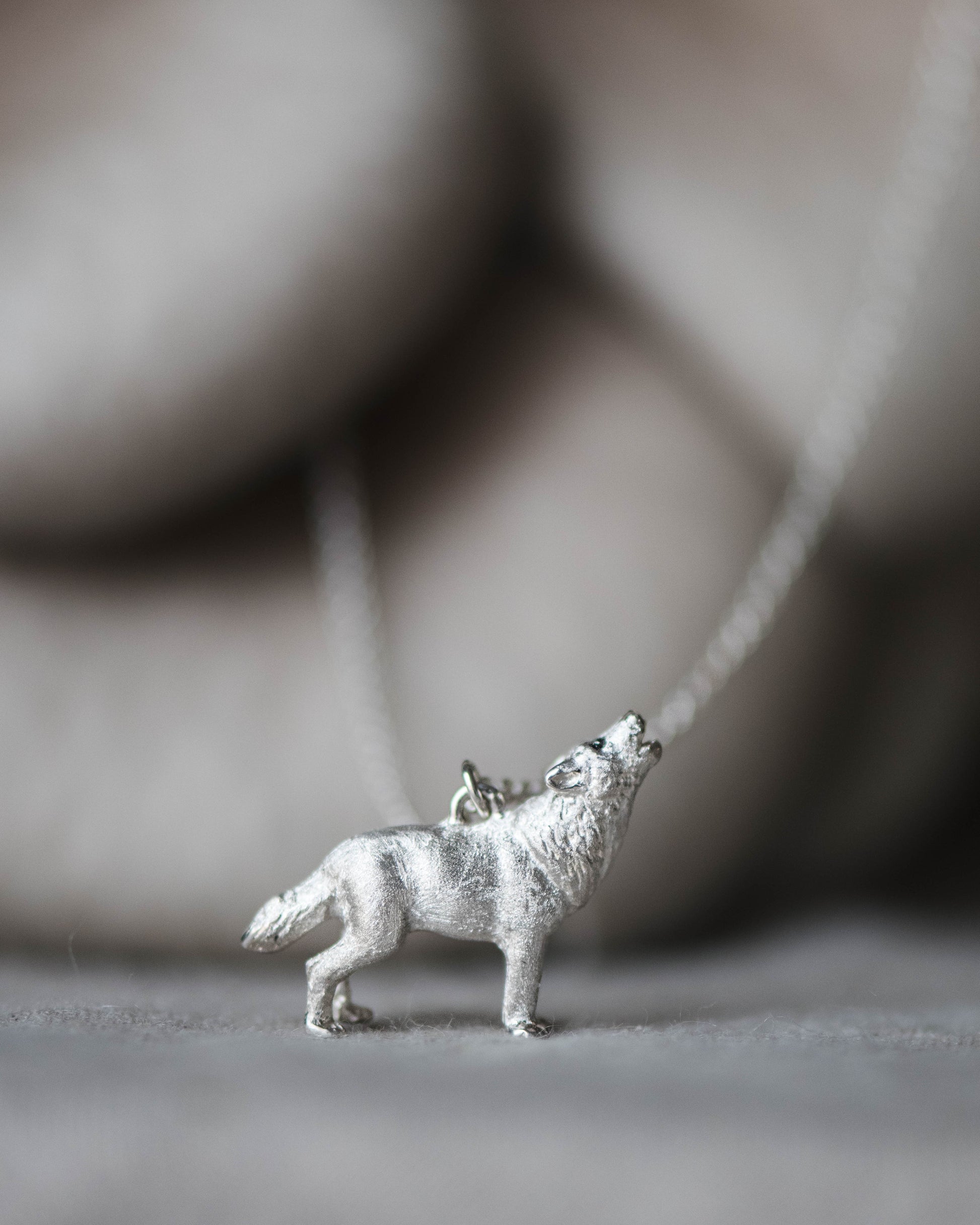 Silver wolf pendant on a chain against a neutral background