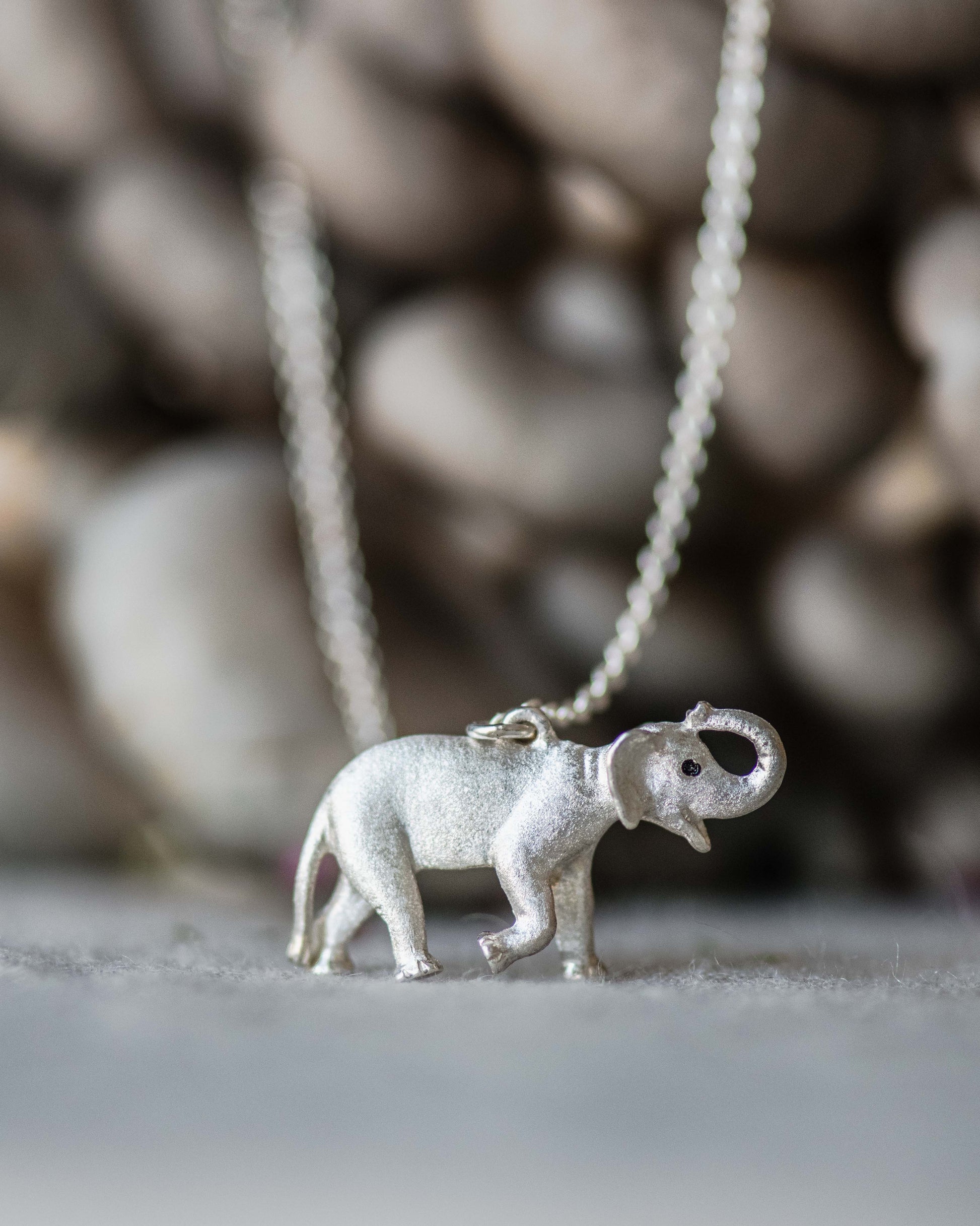 Silver elephant pendant on a chain against a blurred mushroom background