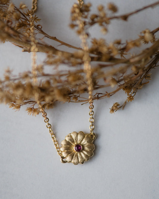Delicate gold bracelet with a daisy pendant and ruby on a light gray background