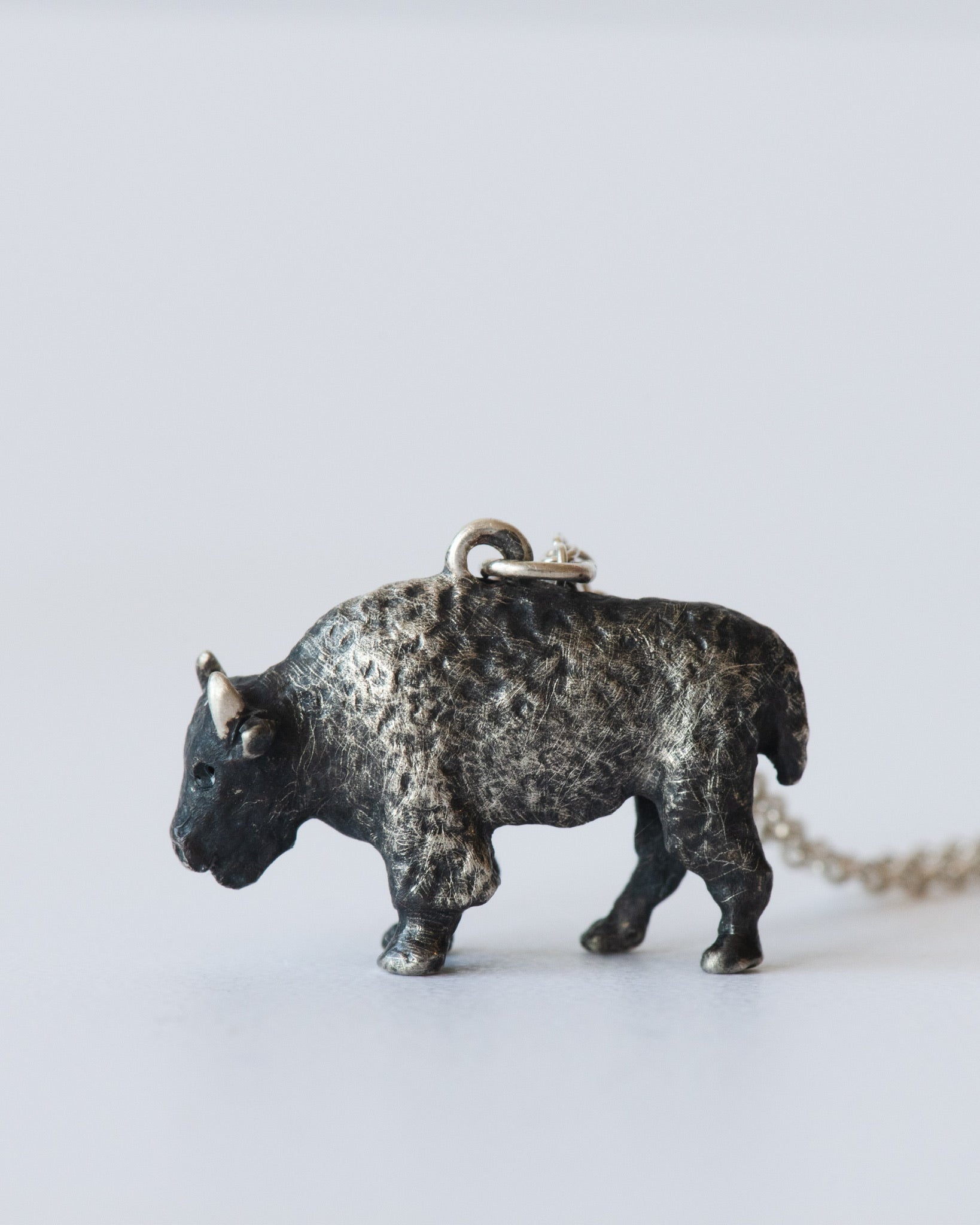Bronze buffalo pendant on a chain against a light gray background