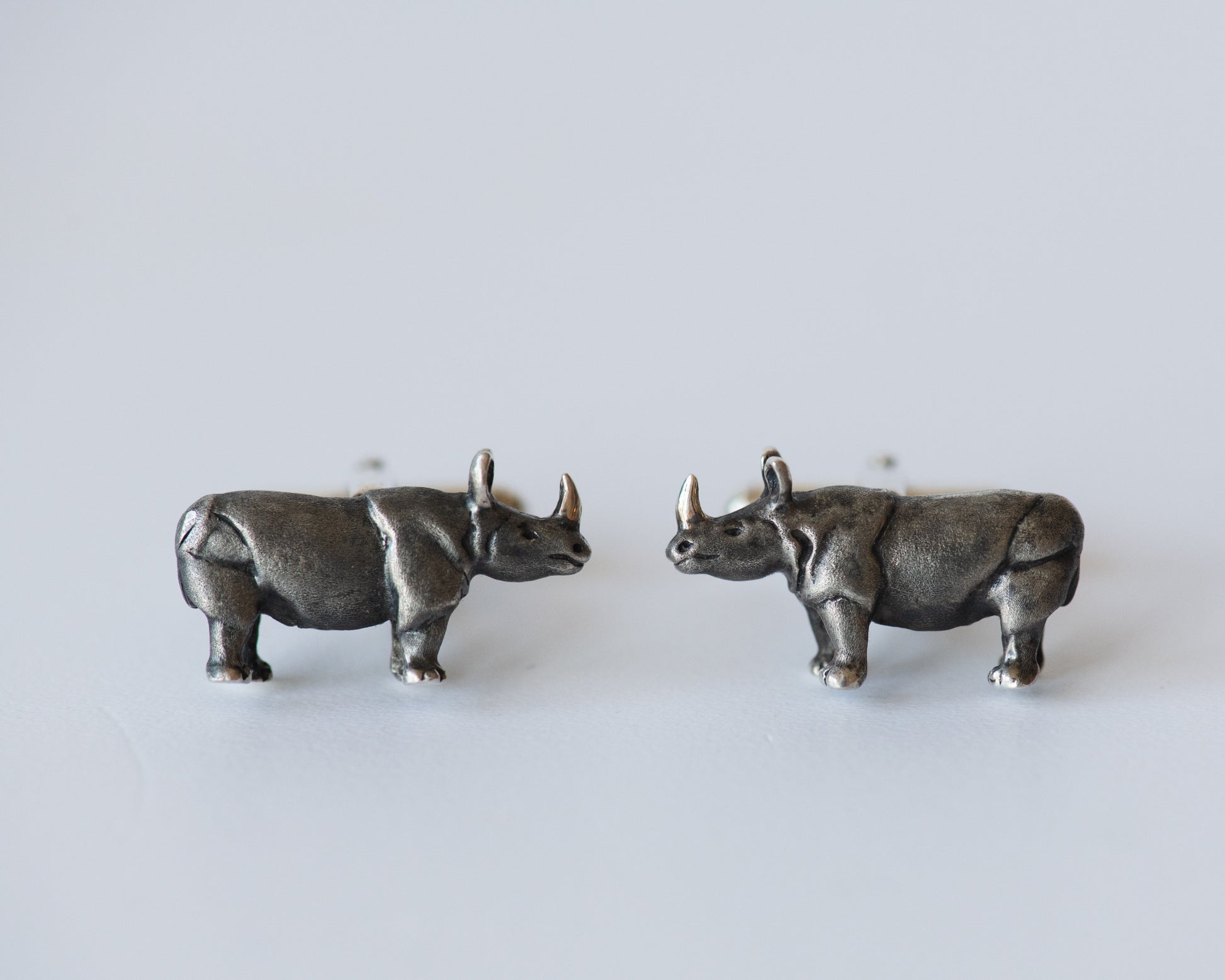 Pair of silver rhinoceros earrings on a light gray background