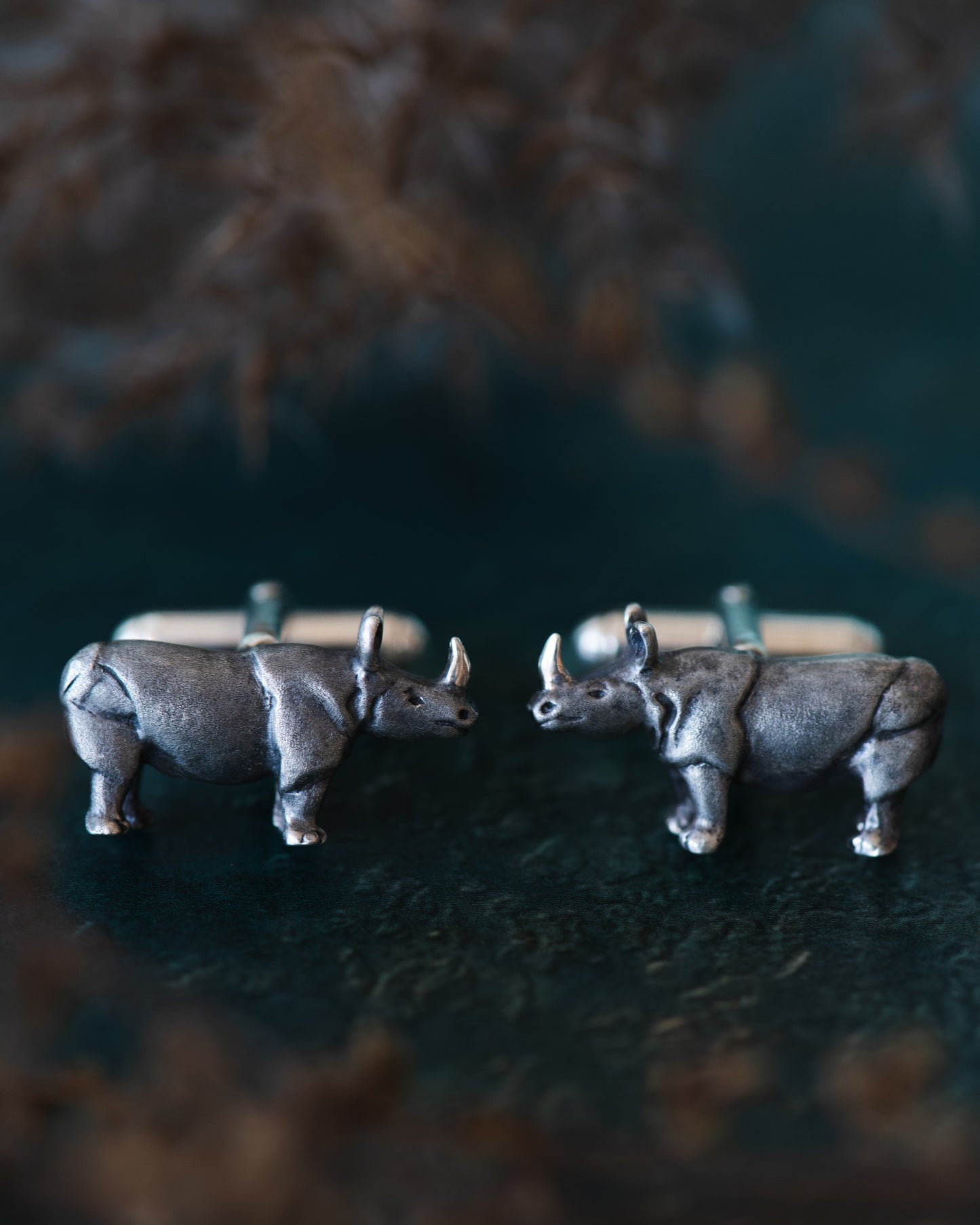 Silver rhinoceros cufflinks on a dark surface with blurred background