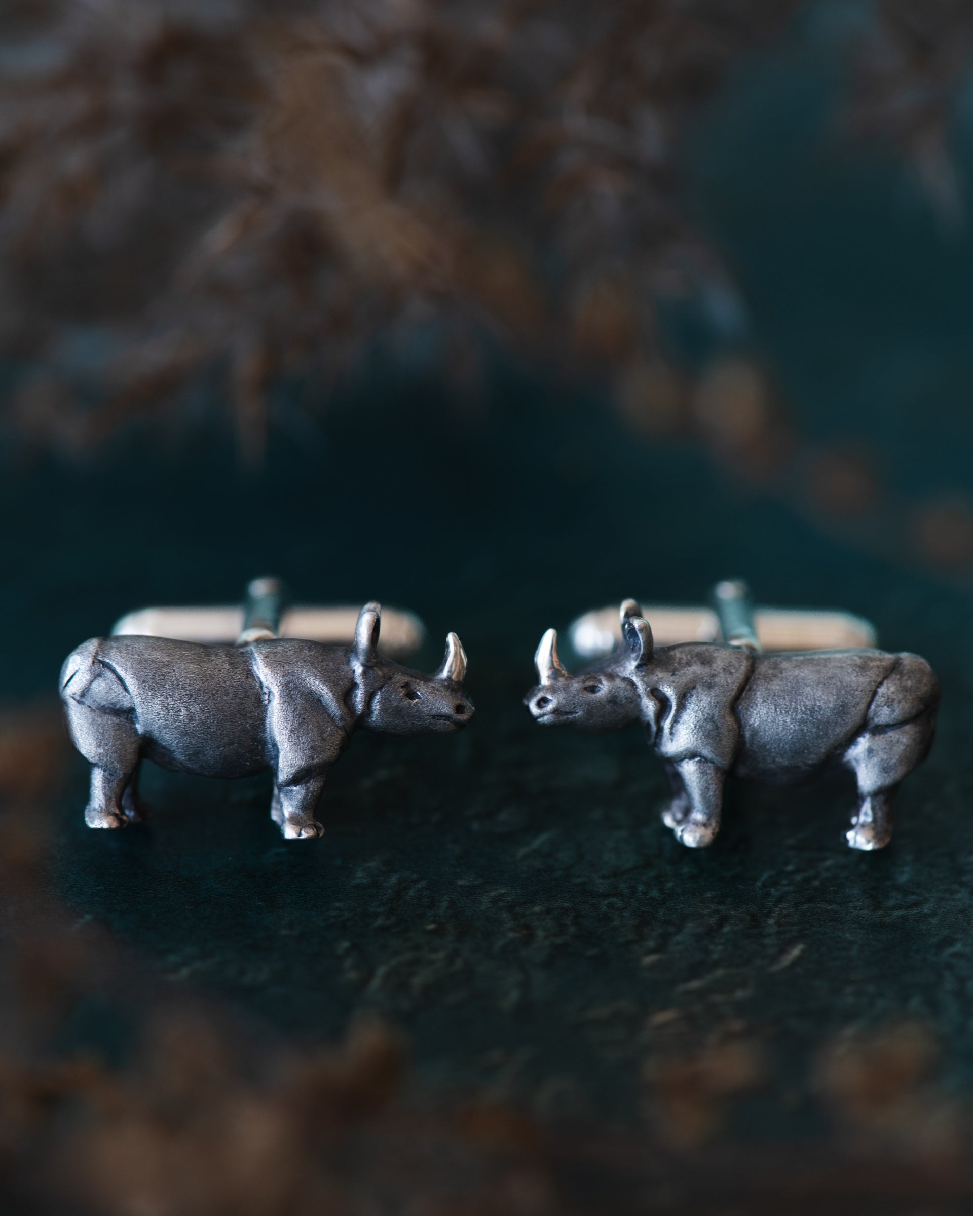 Silver rhinoceros cufflinks on a dark surface with blurred background