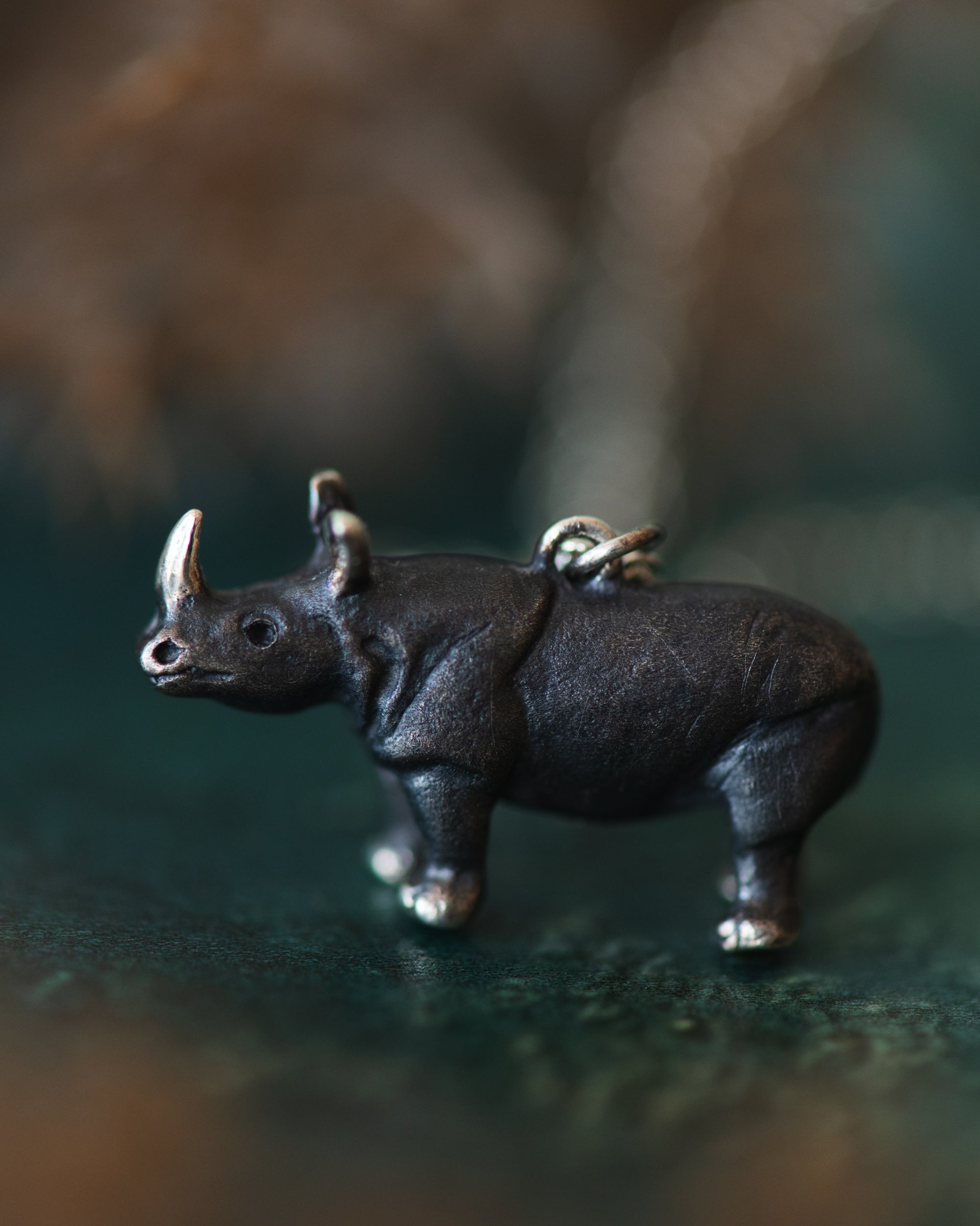 Sterling silver rhinoceros figurine on a dark surface with a blurred background
