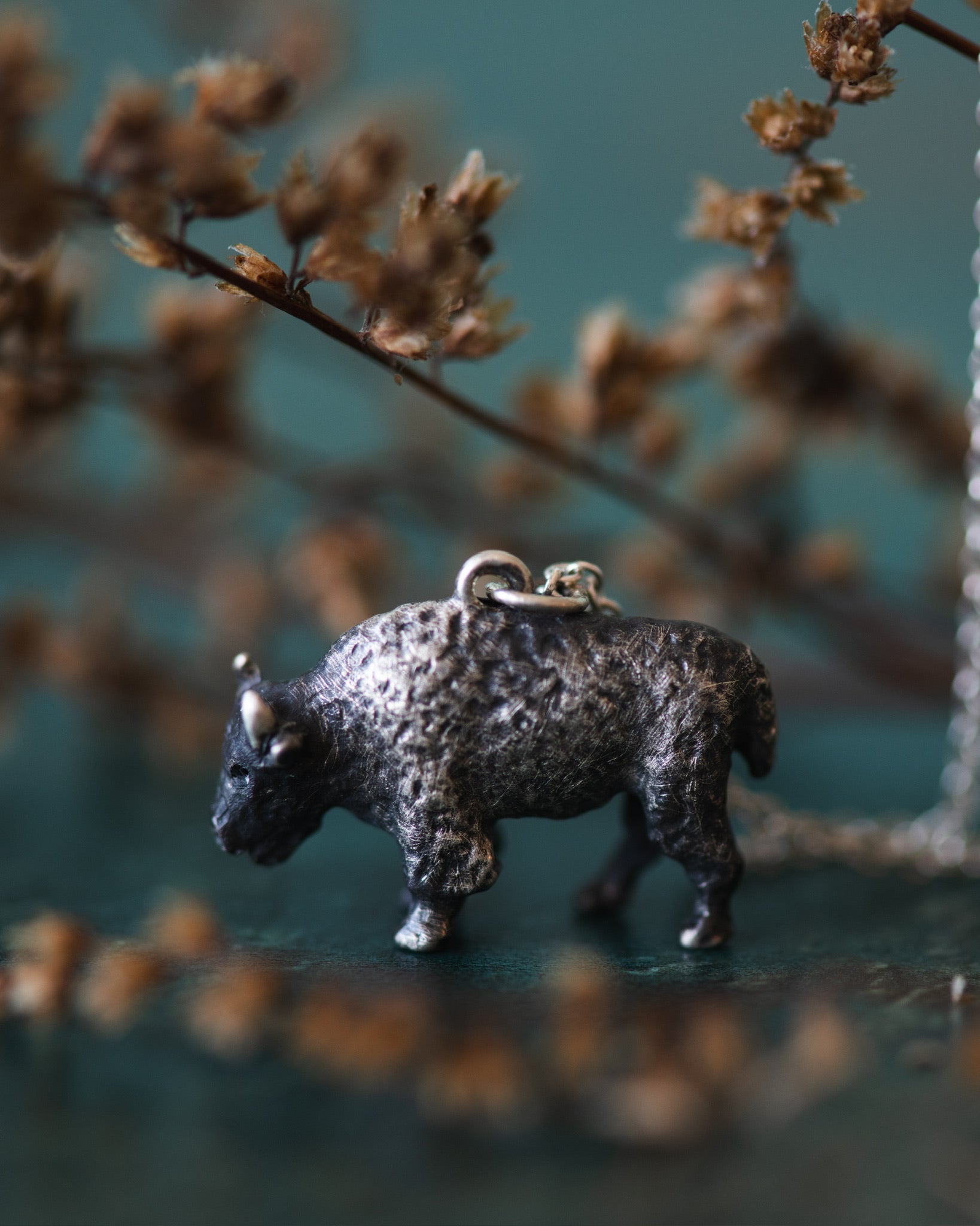 Silver bison pendant on a chain with a blurred natural background