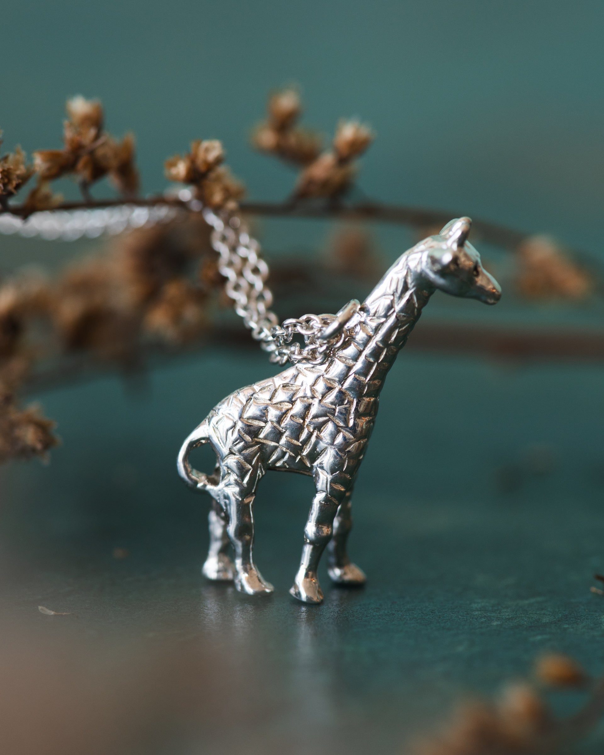 Silver giraffe pendant on a chain against a blurred natural background