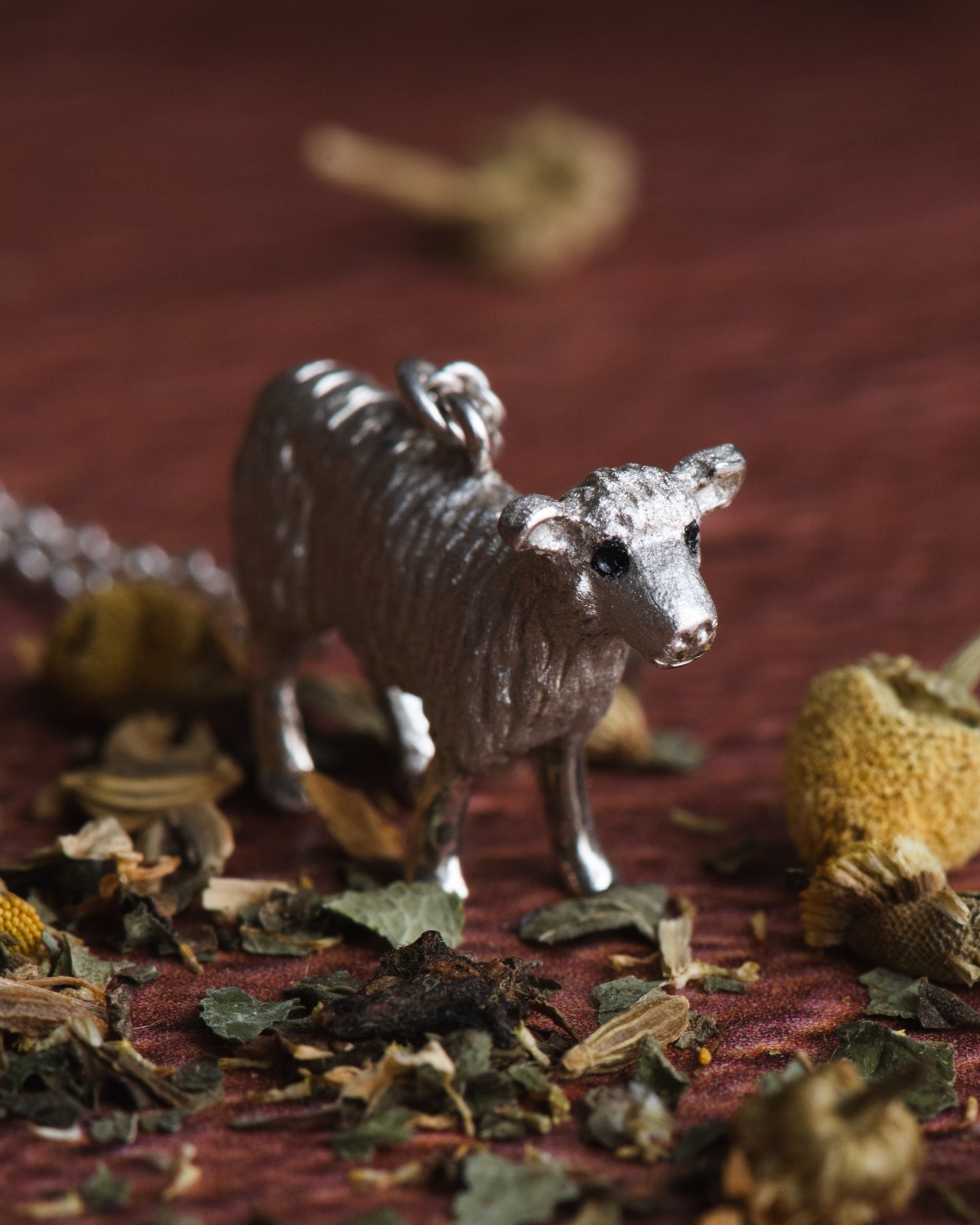 Hand carved sheep figurine in sterling silver on a textured surface with dried leaves