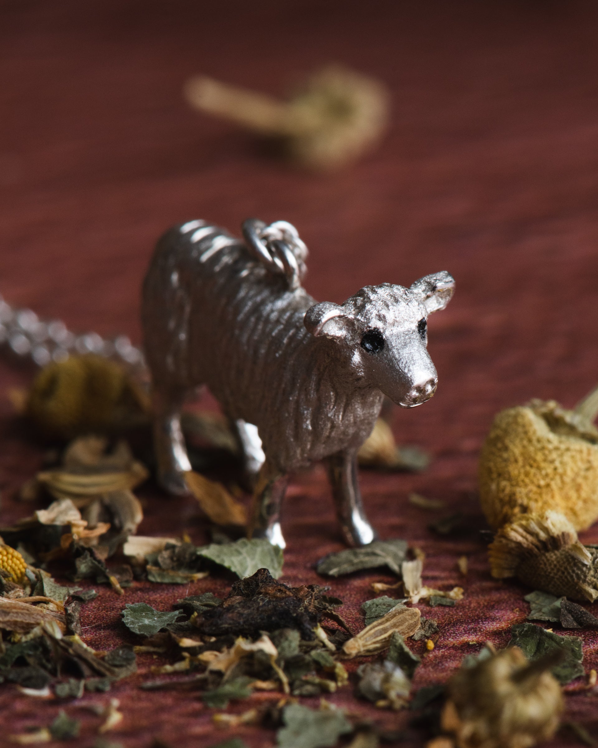 Hand carved sheep figurine in sterling silver on a textured surface with dried leaves