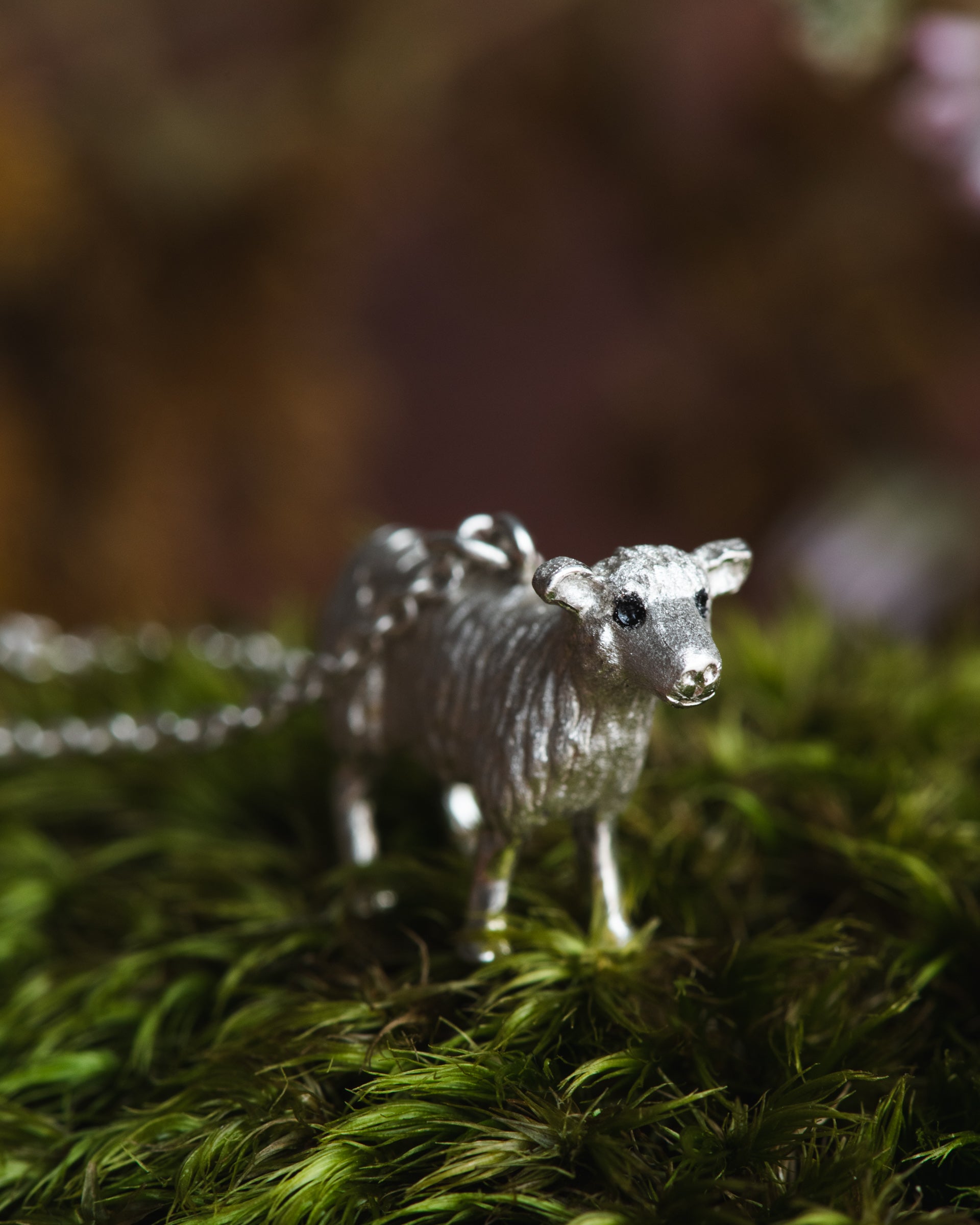 Silver animal figurine on a bed of green moss with a blurred natural background