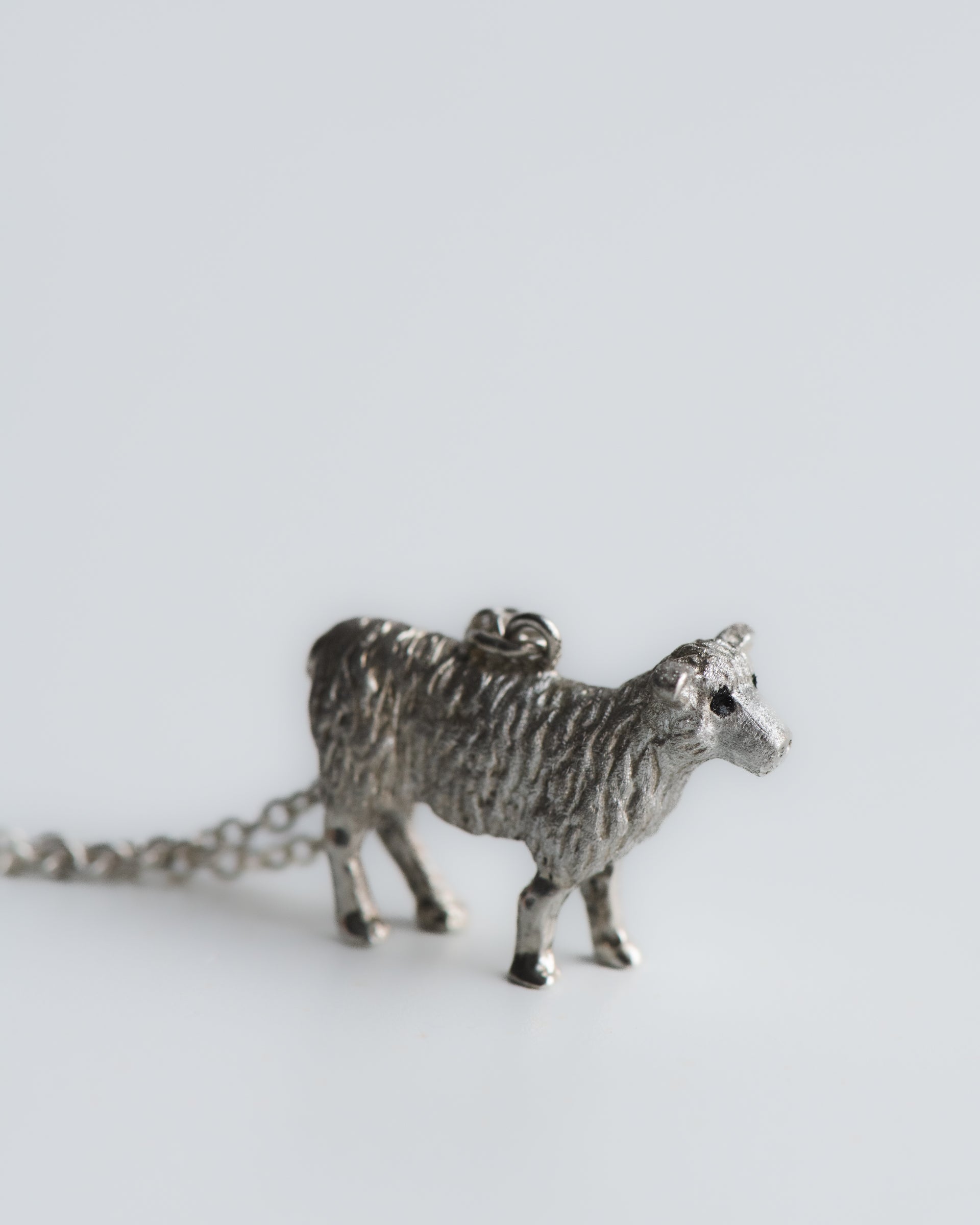 Hand carved Silver sheep pendant on a chain against a white background