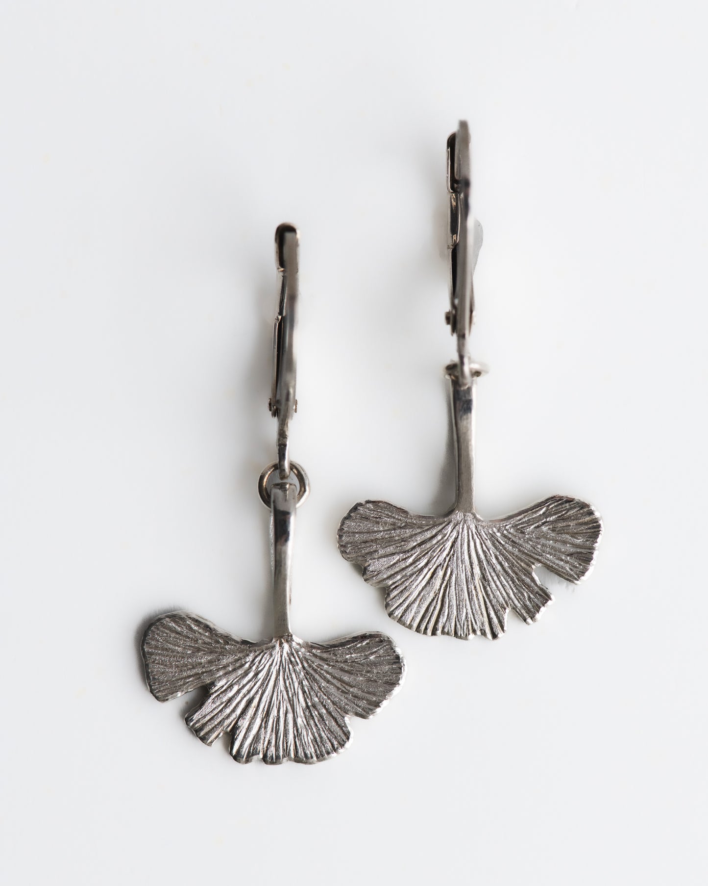 Pair of silver ginkgo leaf earrings on a white background