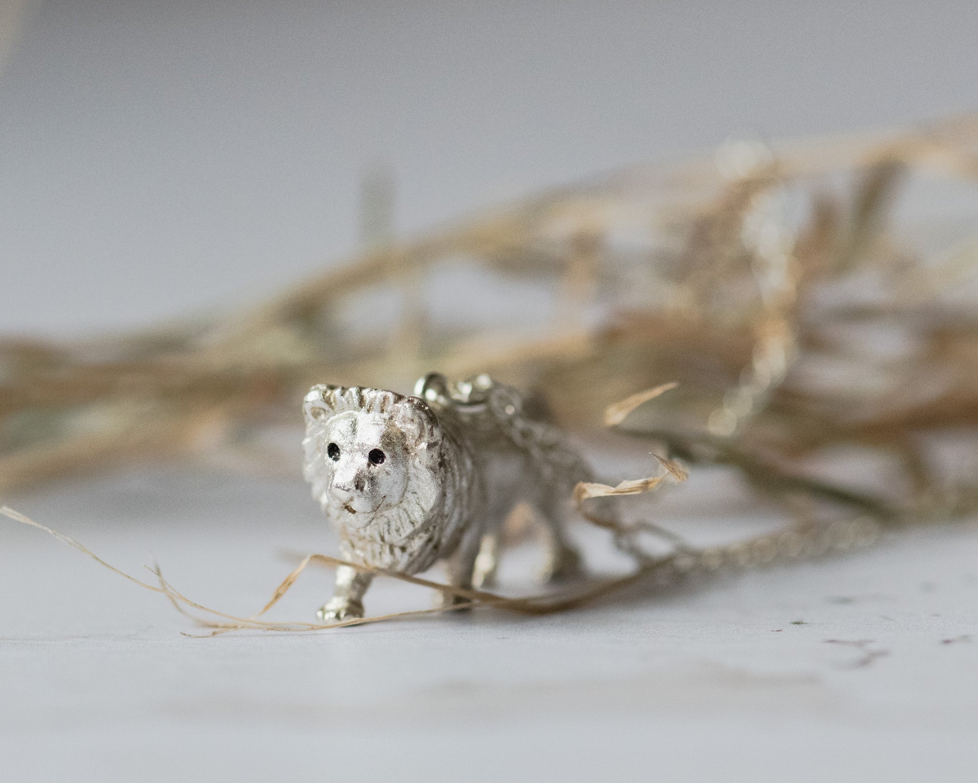 Silver lion figurine on a light background with dry grass