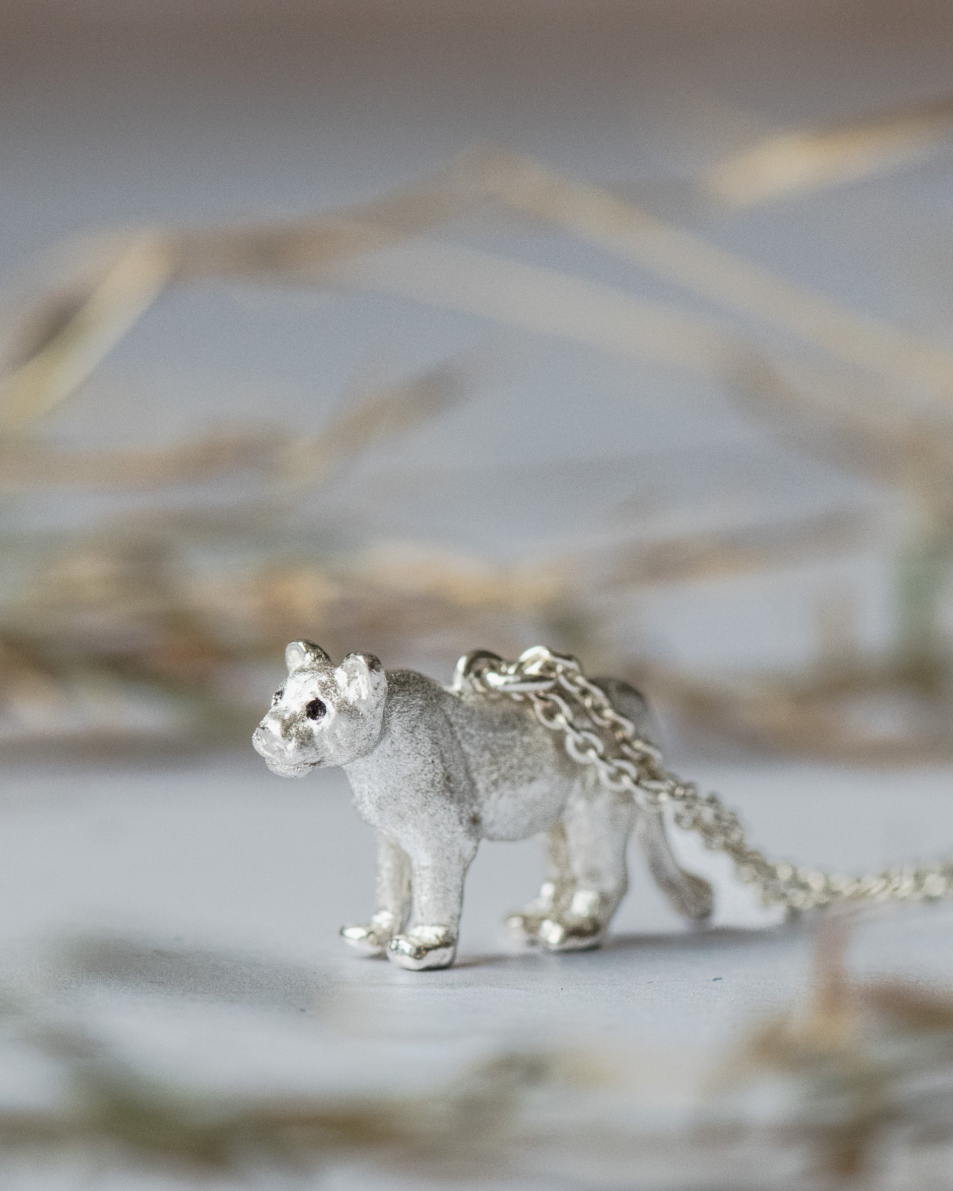 Silver lioness pendant on a chain against a blurred natural background