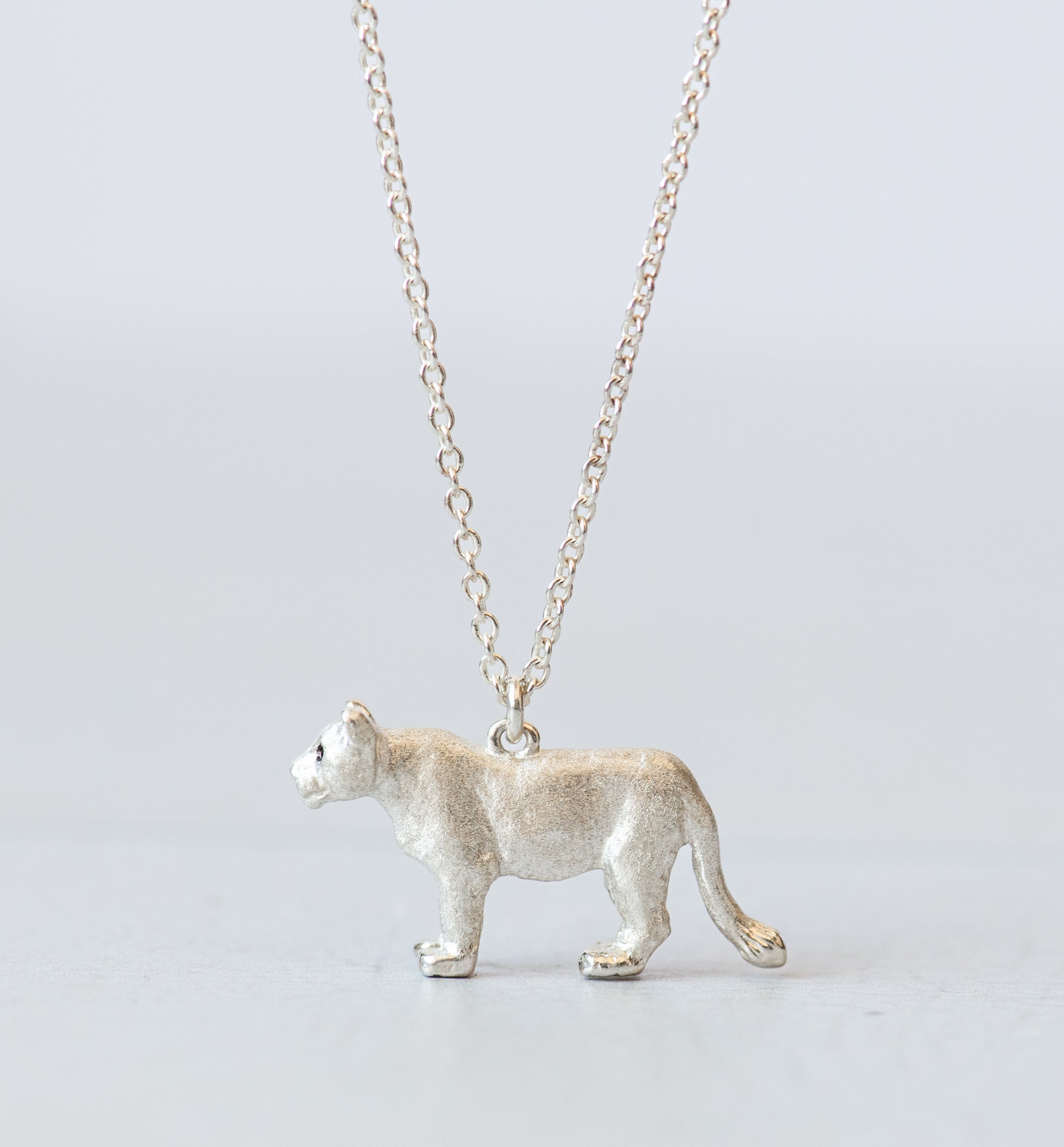 Silver lioness pendant on a chain against a light gray background