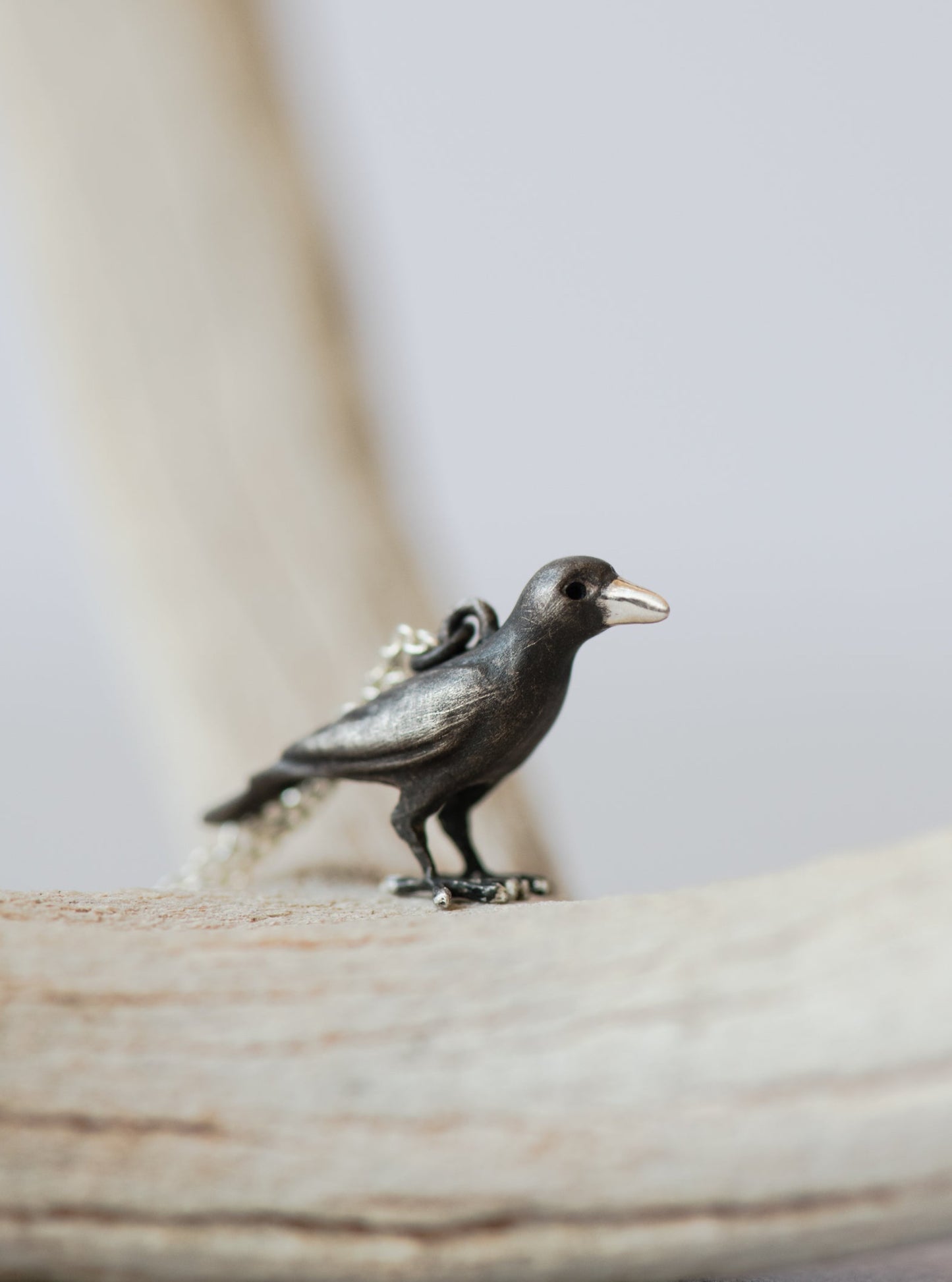 Silver raven pendant on a chain against a neutral background