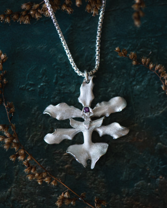 Silver pendant with a purple gemstone on a chain against a dark green background